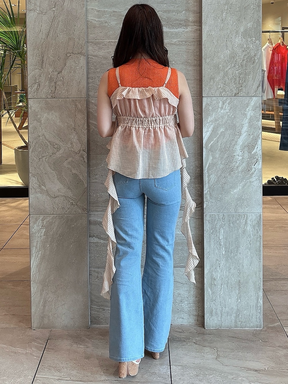 ブルー系のデニムパンツ、オレンジ系のニット/セーター、オレンジ系のキャミソールを着用したレディースの夏コーディネートの4枚目の写真