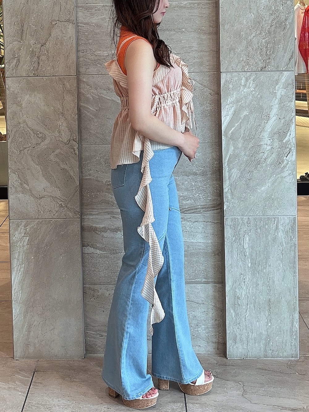 ブルー系のデニムパンツ、オレンジ系のニット/セーター、オレンジ系のキャミソールを着用したレディースの夏コーディネートの2枚目の写真