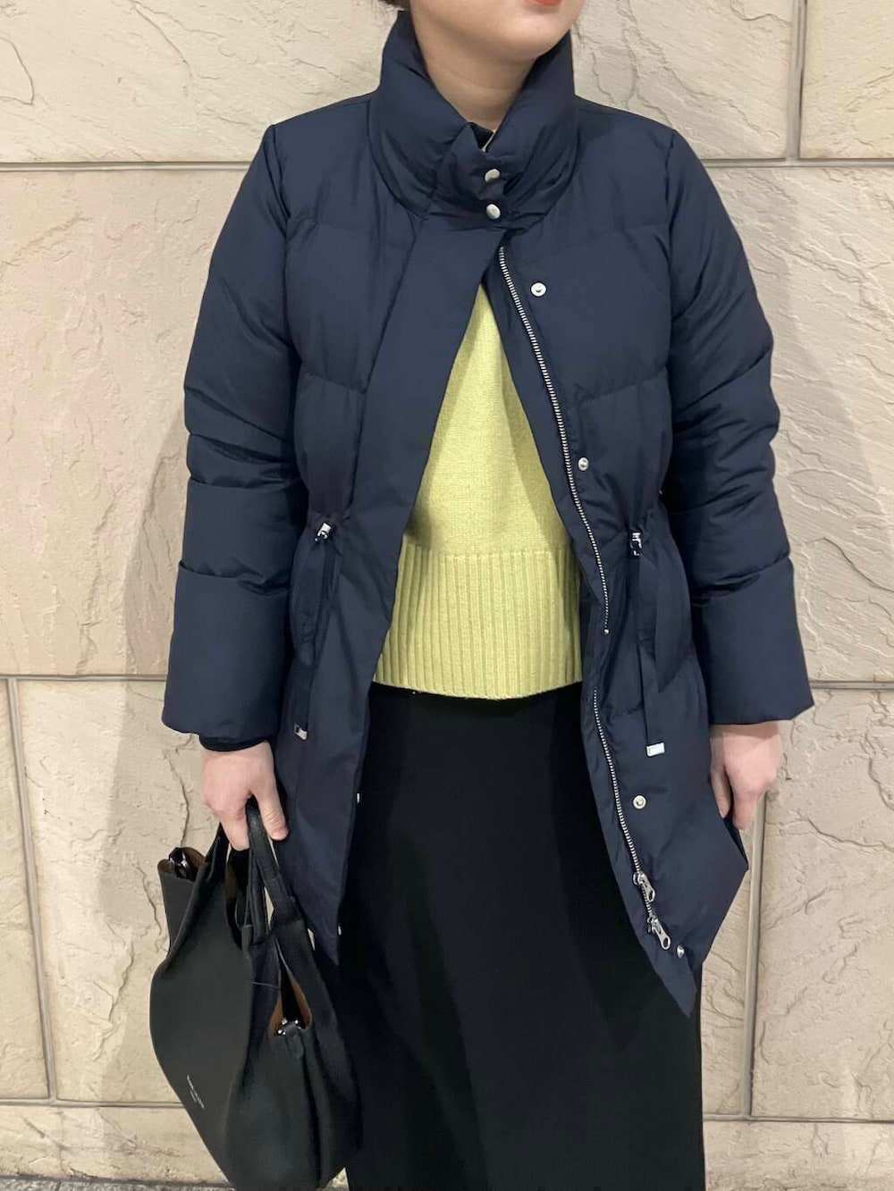 イエロー系のニット/セーター、ブラック系のスカート、ブルー系のダウンジャケット/コートを着用したレディースの冬コーディネートの4枚目の写真