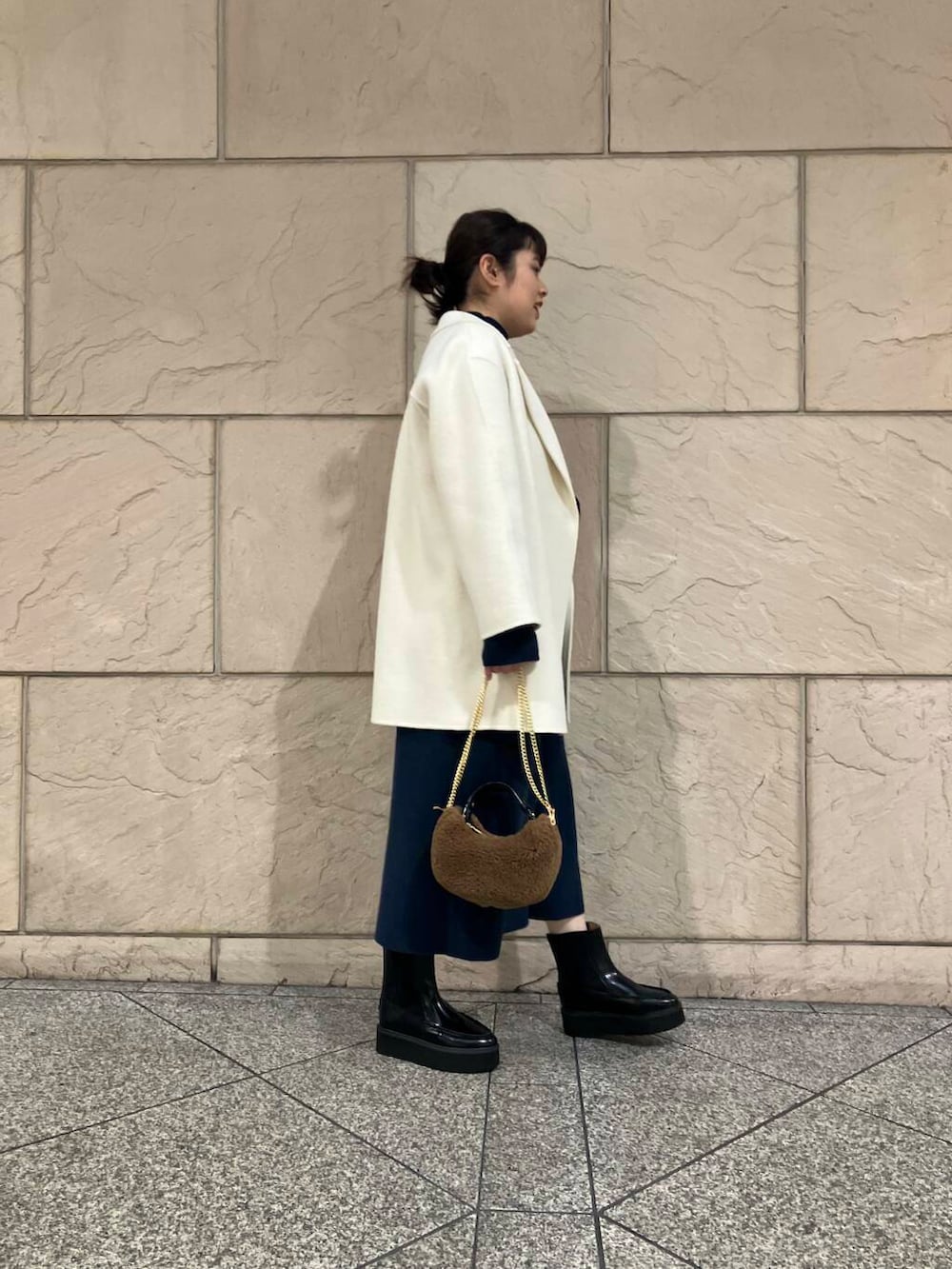 ホワイト系のチェスターコート、ブルー系のワンピース、ブラウン系のショルダーバッグを着用したレディースの冬コーディネートの2枚目の写真