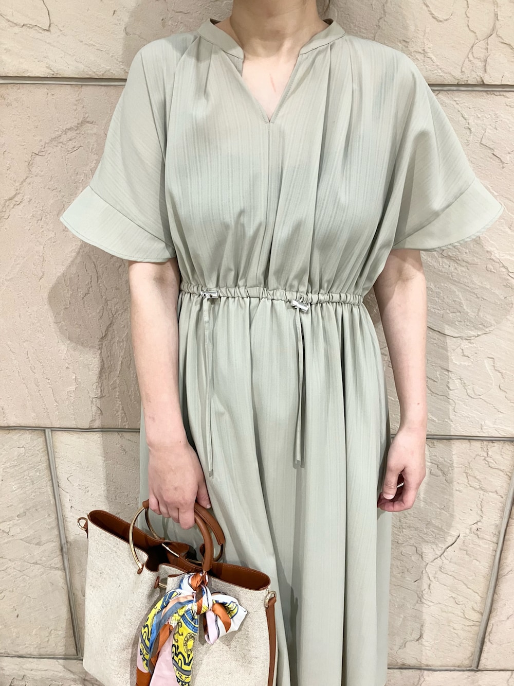 グリーン系のワンピース、ブラウン系のハンドバッグ、ベージュ系のパンプスを着用したレディースの春コーディネートの3枚目の写真