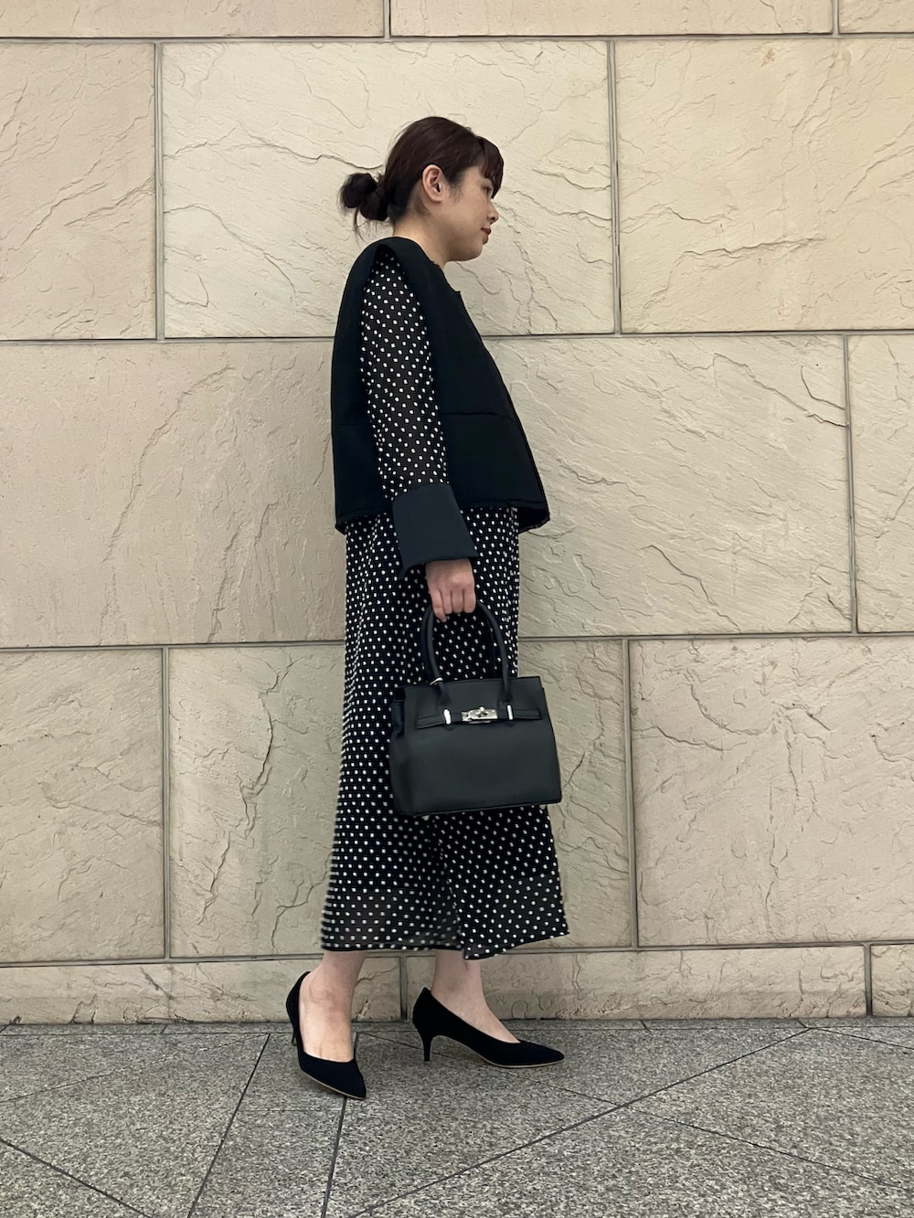 ブラック系のベスト、ブラック系のワンピース、ブラック系のパンプスを着用したレディースの秋コーディネートの2枚目の写真