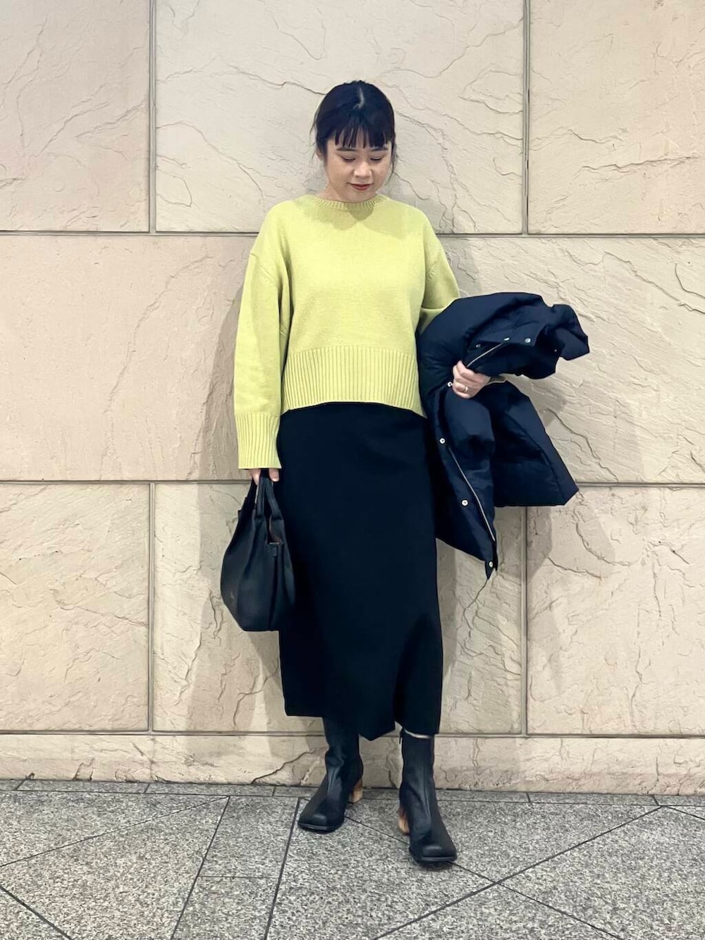 イエロー系のニット/セーター、ブラック系のスカート、ブルー系のダウンジャケット/コートを着用したレディースの冬コーディネートの6枚目の写真