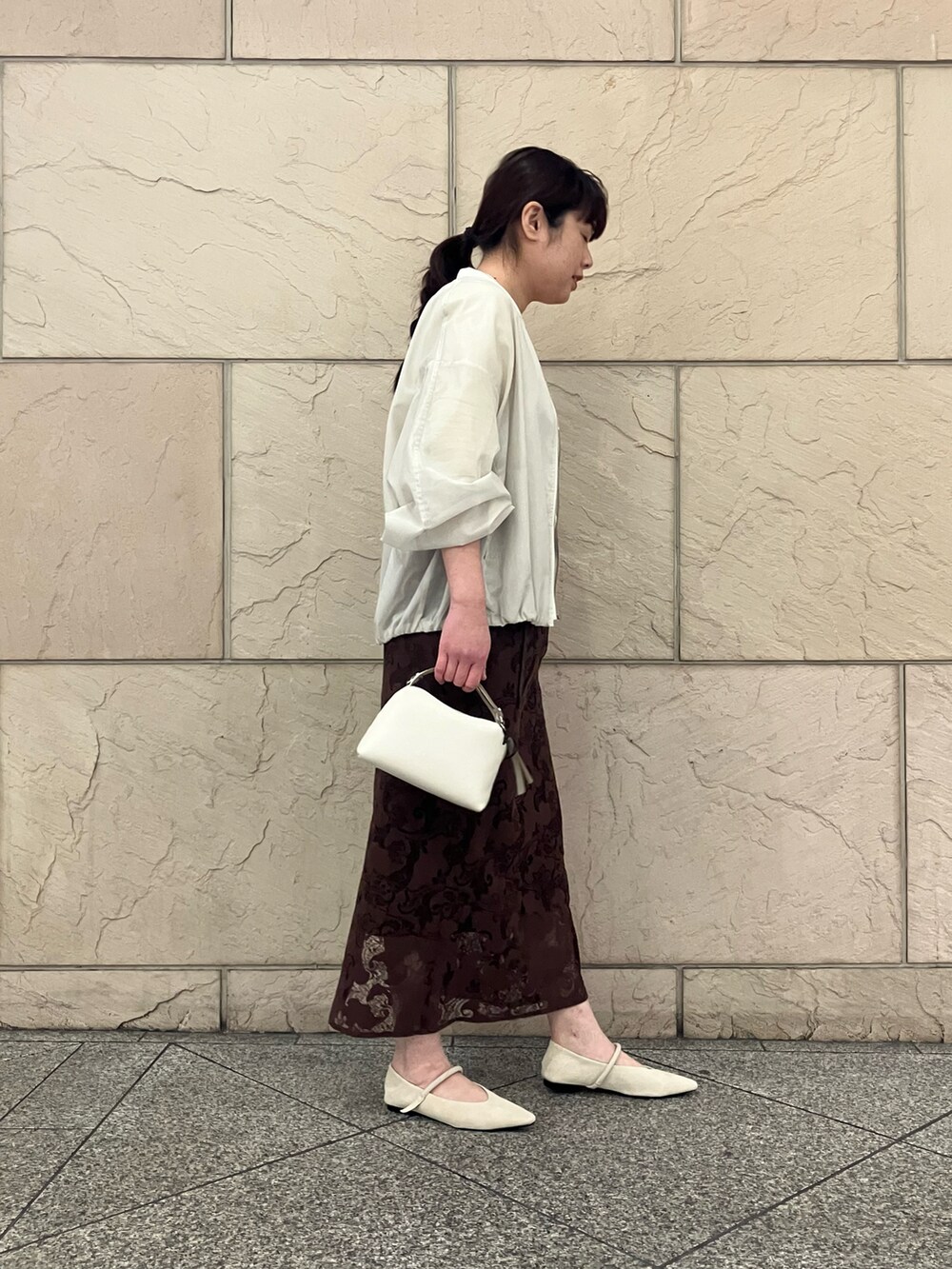 ブラウン系のスカート、ベージュ系のショルダーバッグ、ベージュ系のTシャツ/カットソーを着用したレディースの春コーディネートの2枚目の写真