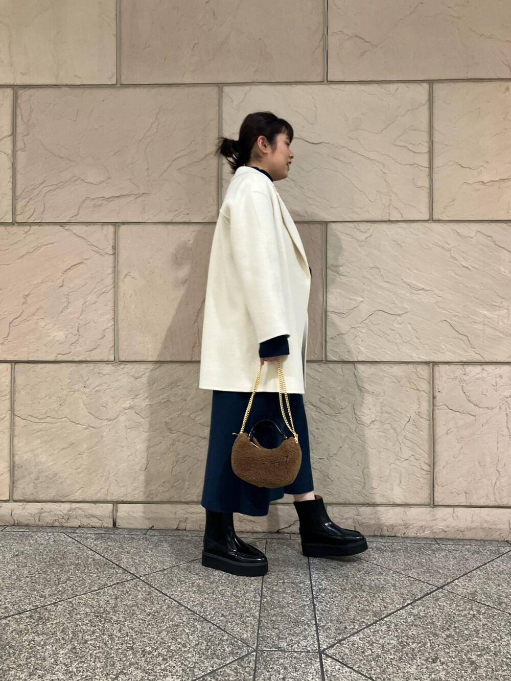 ホワイト系のチェスターコート、ブルー系のワンピース、ブラック系のブーツを着用したレディースの冬コーディネートの2枚目の写真
