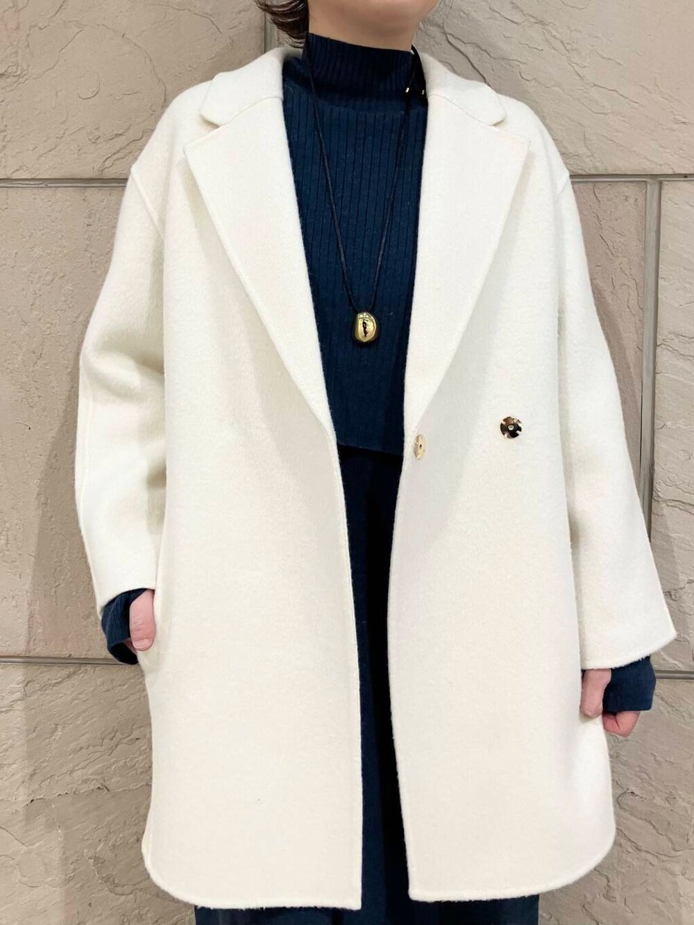 ホワイト系のチェスターコート、ブルー系のワンピース、ブラウン系のショルダーバッグを着用したレディースの冬コーディネートの3枚目の写真