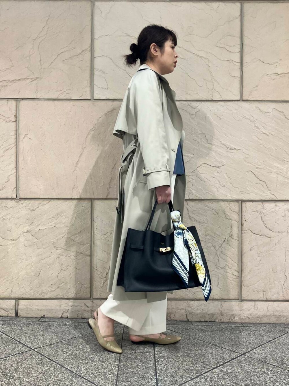 グレー系のトレンチコート、ベージュ系のパンプス、ブラック系のトートバッグを着用したレディースの春コーディネートの2枚目の写真