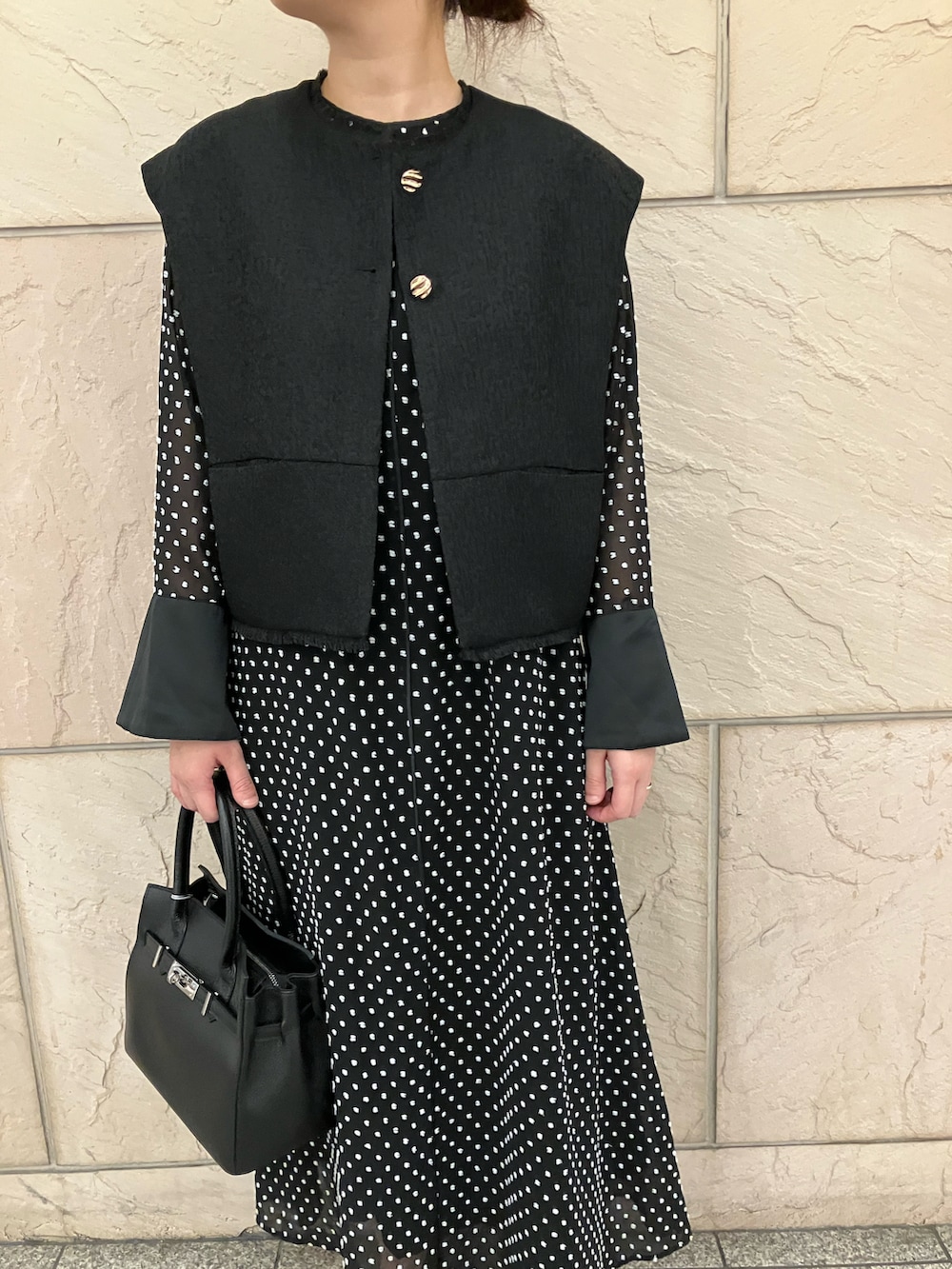 ブラック系のベスト、ブラック系のワンピース、ブラック系のパンプスを着用したレディースの秋コーディネートの4枚目の写真