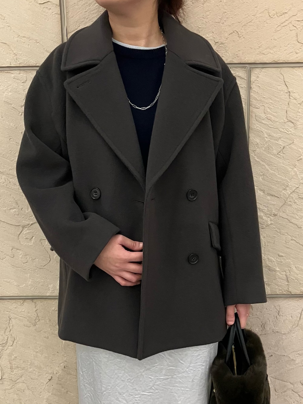 グレー系のニット/セーター、グレー系のピーコート、ブラウン系のハンドバッグを着用したレディースの秋コーディネートの4枚目の写真