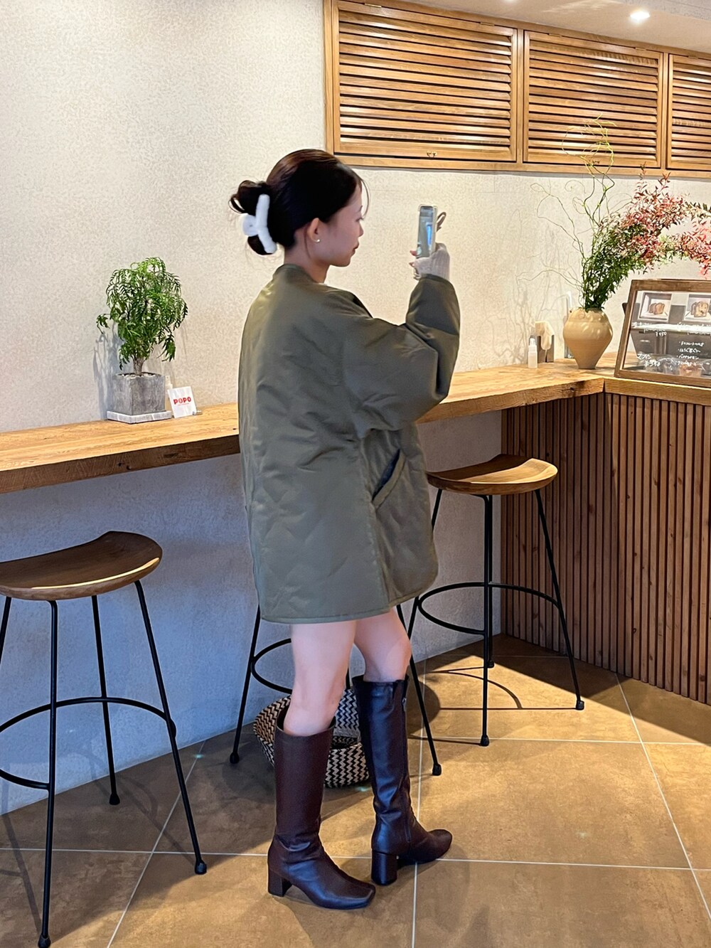 グリーン系のノーカラージャケット、ブラウン系のブーツ、ブラウン系のパンツを着用したレディースの秋コーディネートの2枚目の写真