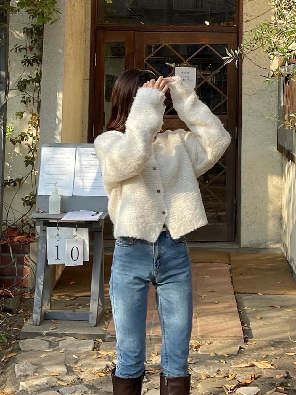 ホワイト系のカーディガン/ボレロ、ブラウン系のブーツ、ブルー系のデニムパンツを着用したレディースの秋コーディネートの3枚目の写真