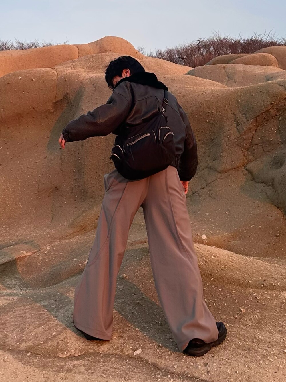 グレー系のスラックス、ブラック系のムートンコート、ブラック系のスニーカーを着用したメンズの春コーディネートの2枚目の写真