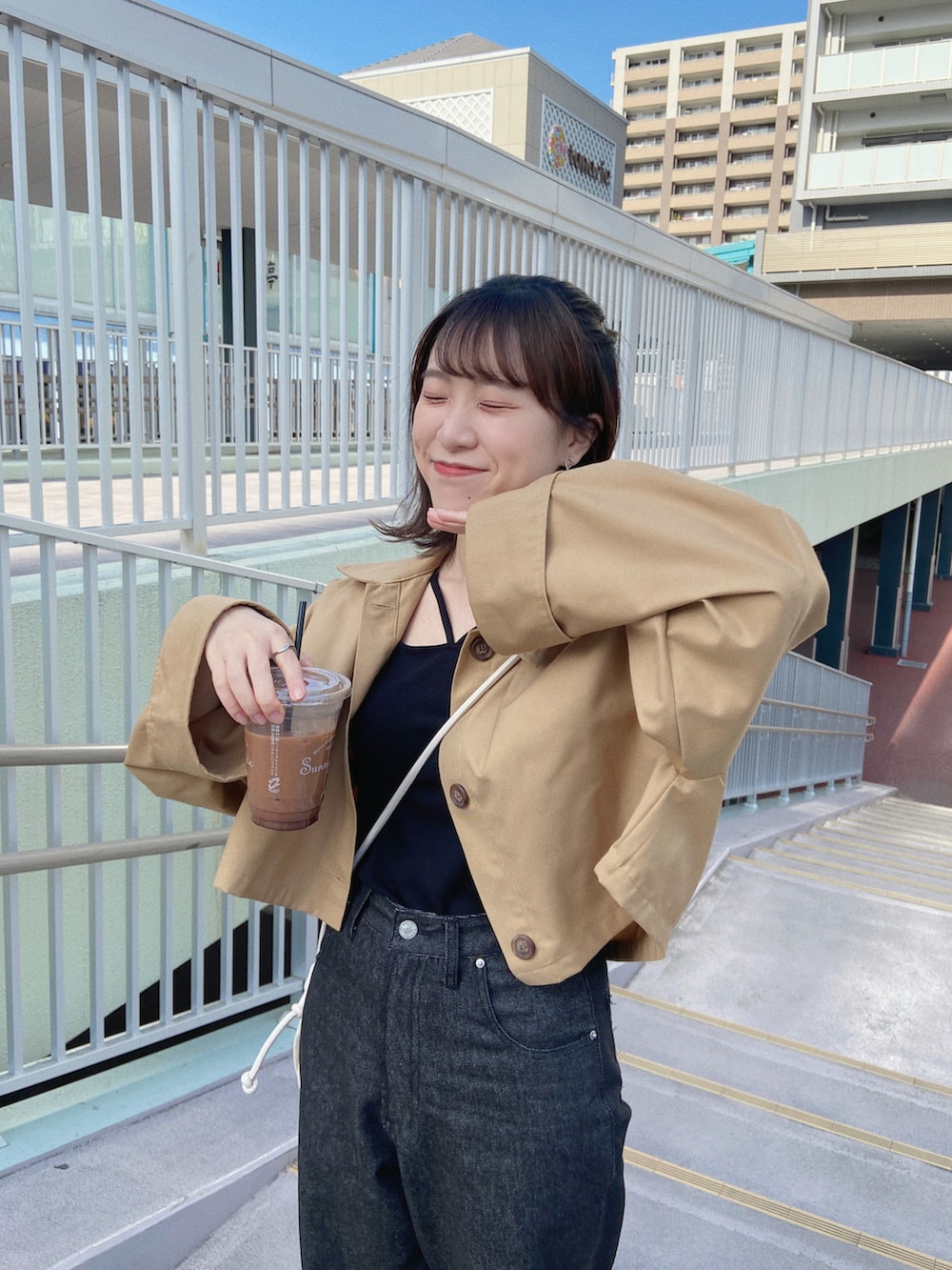 ブラック系のデニムパンツ、ブラック系のスニーカー、ベージュ系のステンカラーコートを着用したレディースの春コーディネートの3枚目の写真