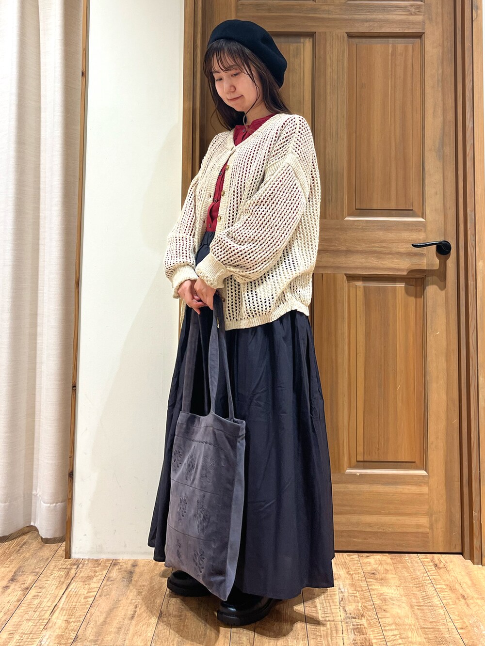 グレー系のハンドバッグ、グレー系のスカート、レッド系のニット/セーターを着用したレディースの秋コーディネートの2枚目の写真