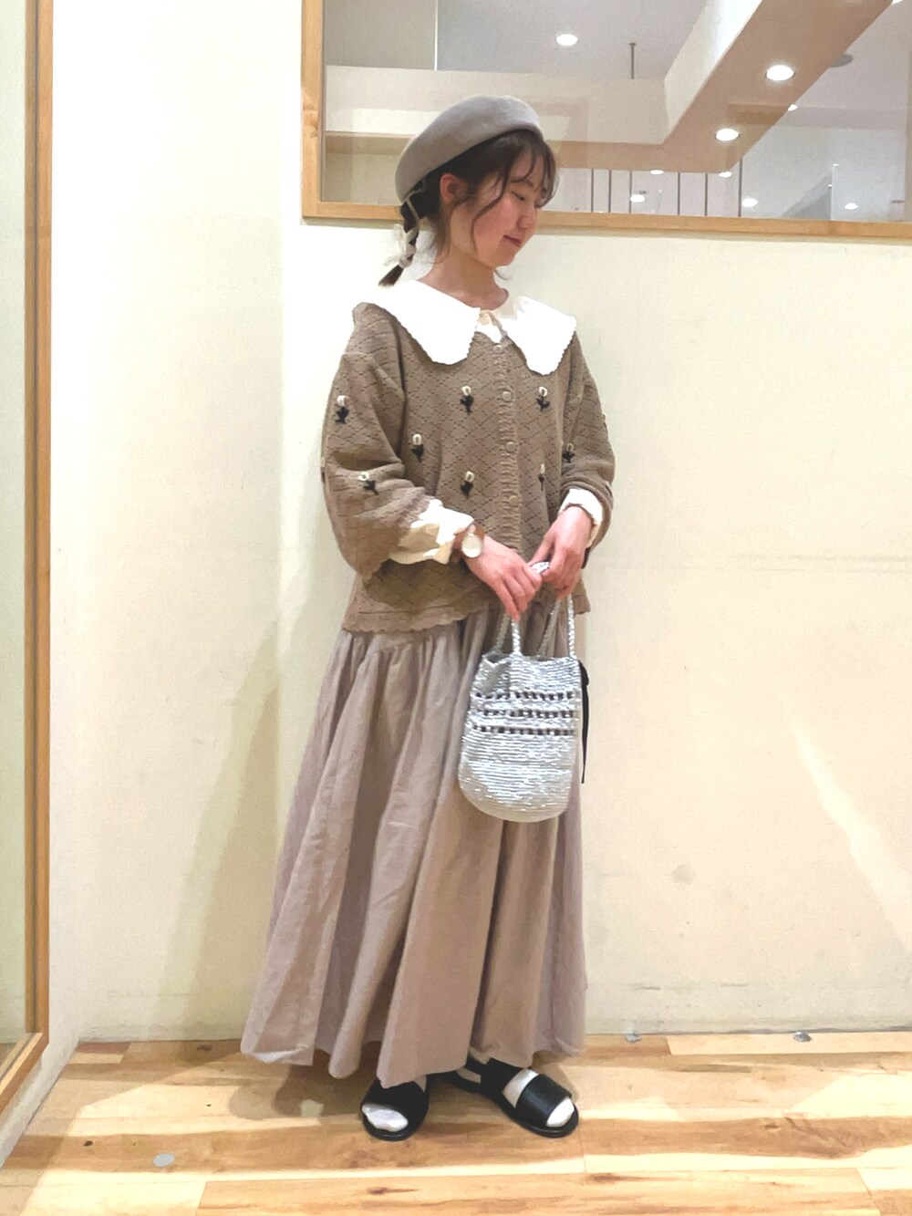 シルバー系のハンドバッグ、ベージュ系のスカート、ブラック系のサンダルを着用したレディースの春コーディネートの2枚目の写真