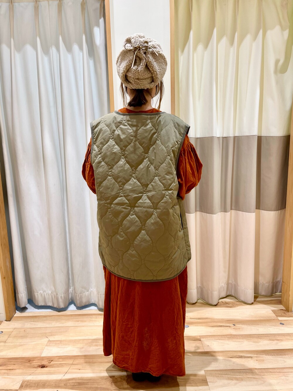 グリーン系のベスト、オレンジ系のワンピース、ベージュ系のキャップを着用したレディースの秋コーディネートの2枚目の写真