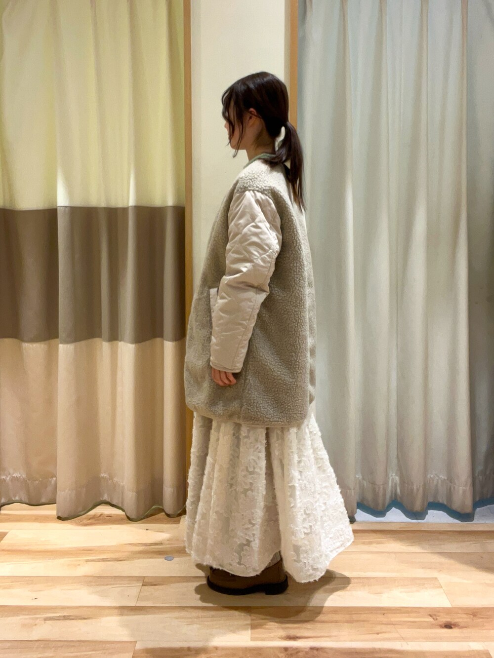 グリーン系のニット/セーター、ホワイト系のスカート、グレー系のその他アウターを着用したレディースの冬コーディネートの2枚目の写真