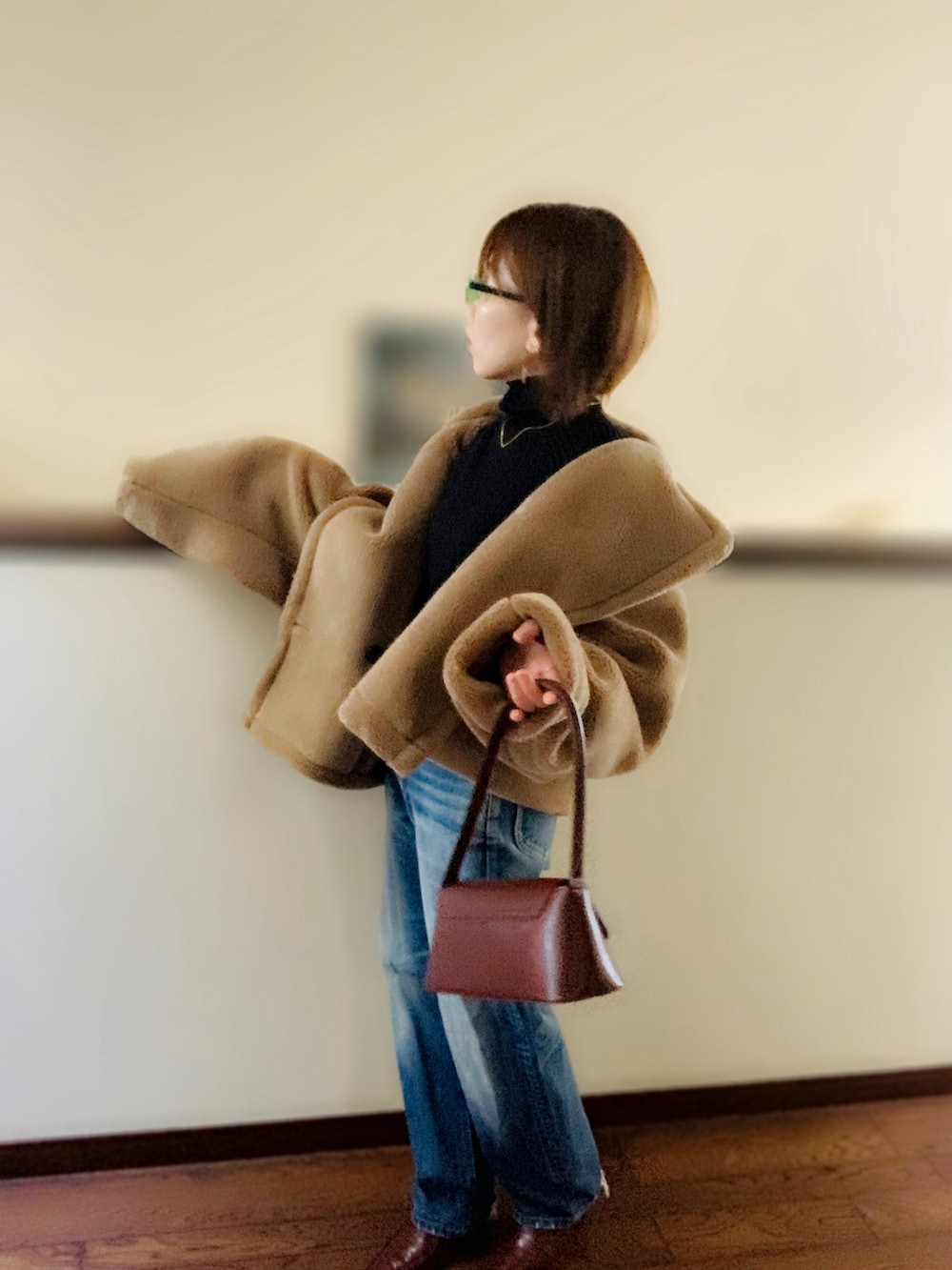 ブラック系のニット/セーター、ブラウン系のその他アウター、ブルー系のデニムパンツを着用したレディースの春コーディネートの2枚目の写真