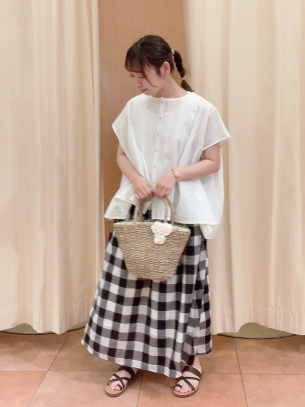 ホワイト系のかごバッグ、ブラウン系のサンダル、ブラック系のスカートを着用したレディースの夏コーディネートの2枚目の写真