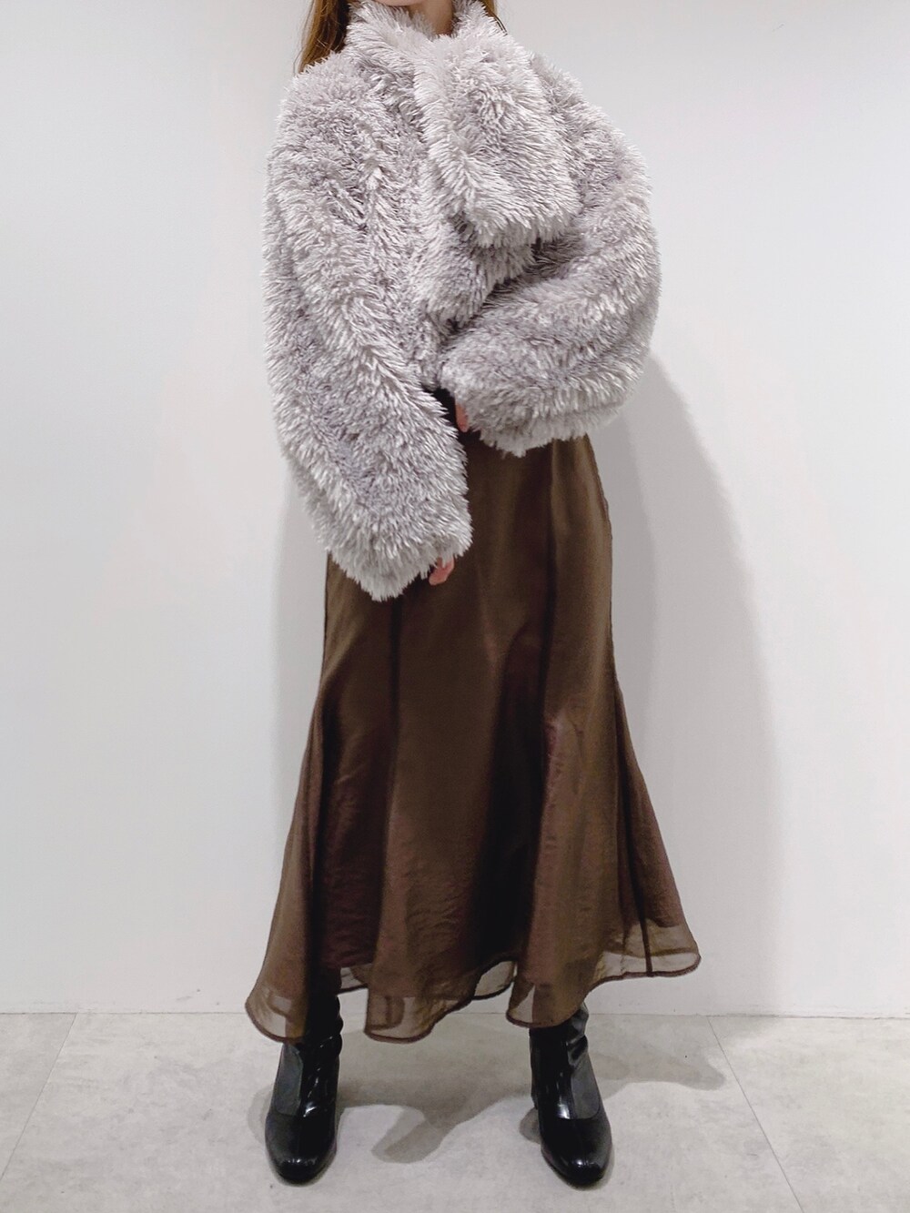 ブラウン系のスカート、ホワイト系のTシャツ/カットソー、ブラック系のブーツを着用したレディースの秋コーディネートの2枚目の写真