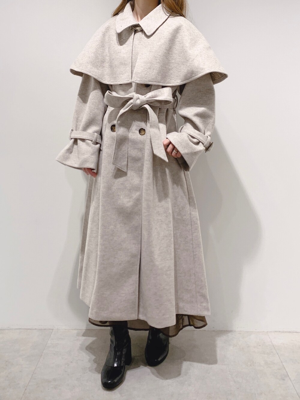 ベージュ系のステンカラーコート、ブラウン系のスカート、ブラック系のブーツを着用したレディースの秋コーディネートの3枚目の写真