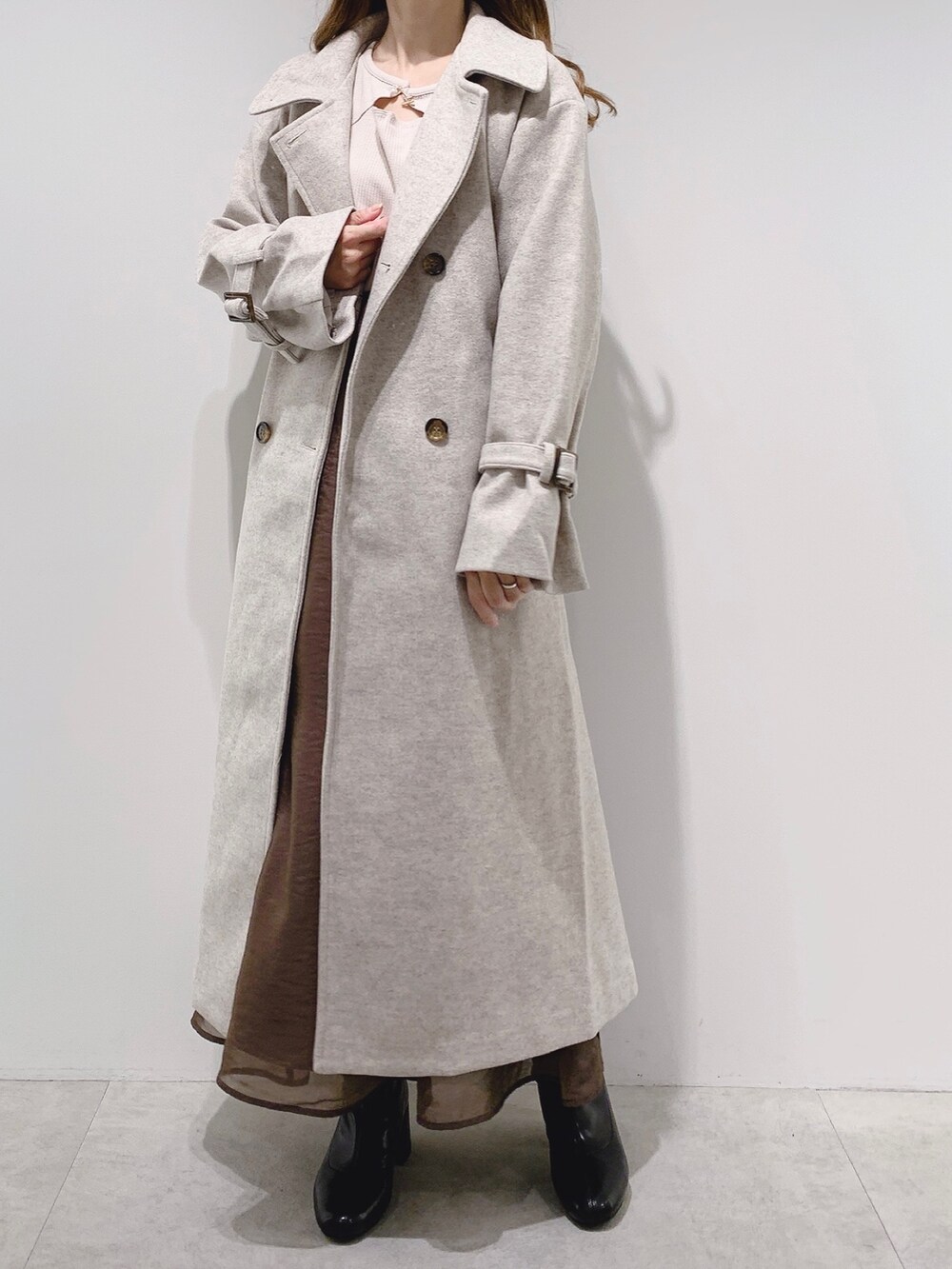 ベージュ系のステンカラーコート、ブラウン系のスカート、ブラック系のブーツを着用したレディースの秋コーディネートの2枚目の写真