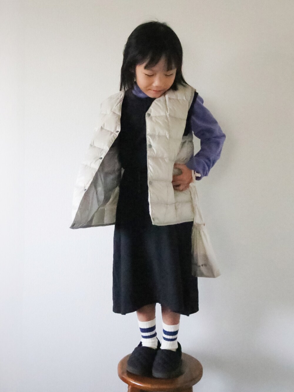 ブラック系のワンピース、ホワイト系のダウンベスト、パープル系のトップスを着用したキッズの冬コーディネートの2枚目の写真