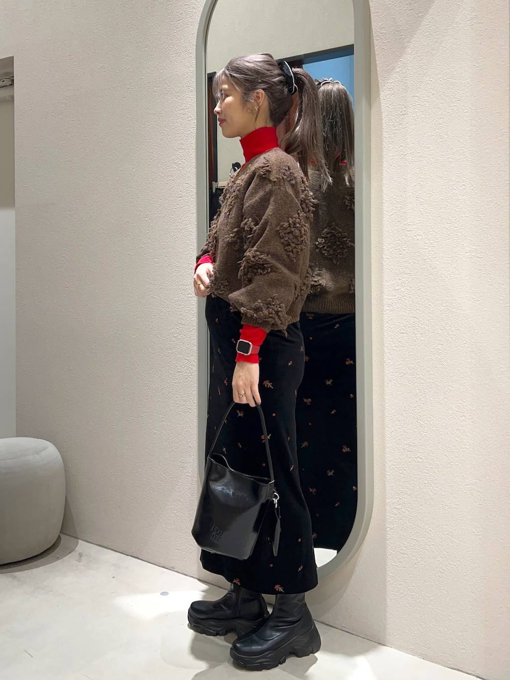 レッド系のニット/セーター、ブラック系のブーツ、ブラック系のスカートを着用したレディースの冬コーディネートの2枚目の写真