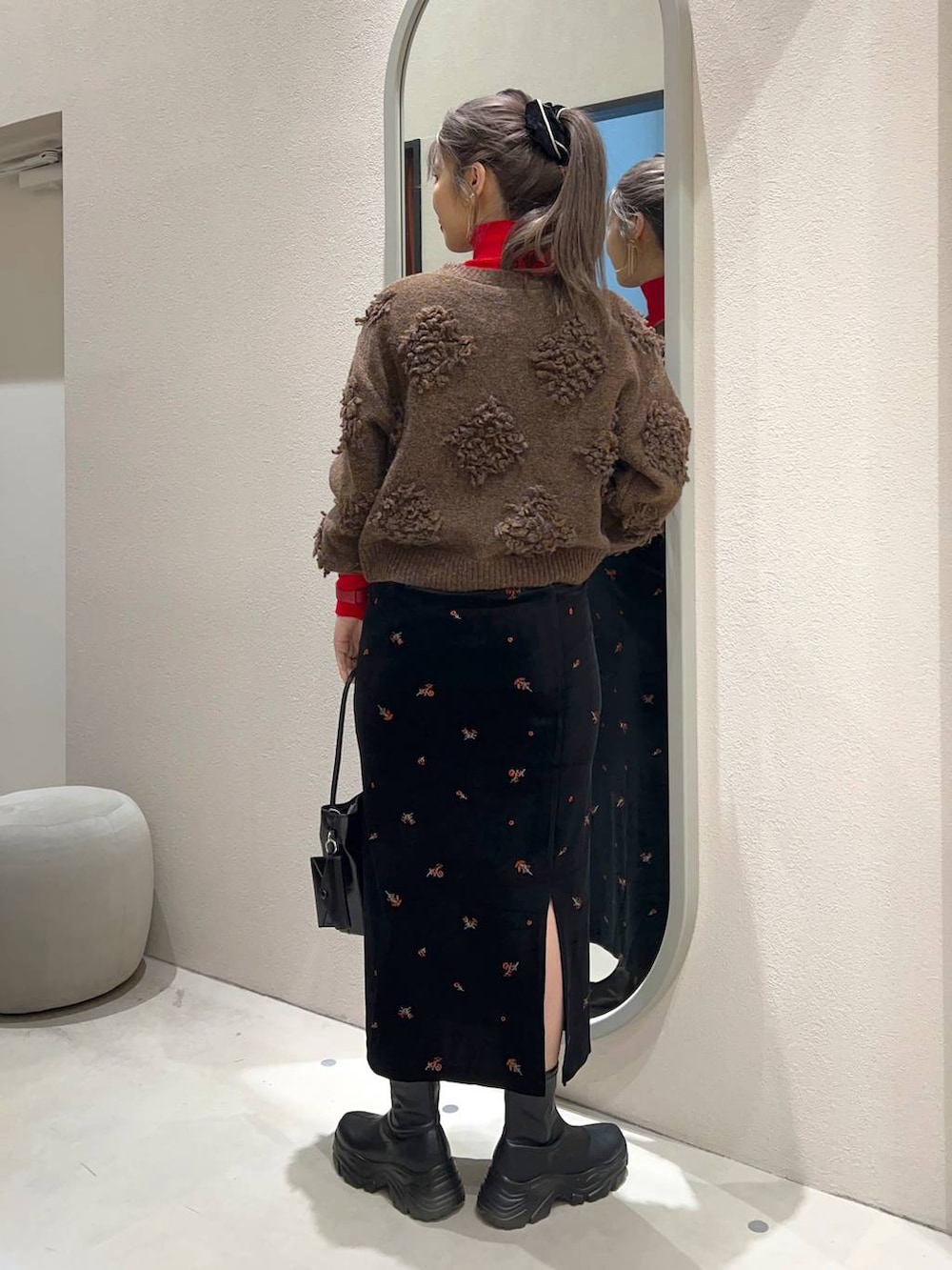 レッド系のニット/セーター、ブラック系のブーツ、ブラック系のスカートを着用したレディースの冬コーディネートの3枚目の写真