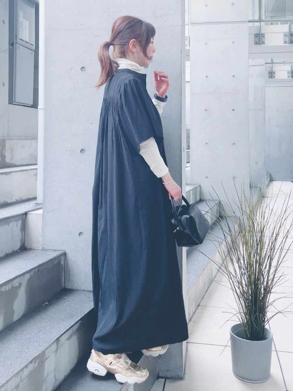 ブラック系のワンピース、ブラック系のハンドバッグ、ゴールド系のスニーカーを着用したレディースの春コーディネートの2枚目の写真