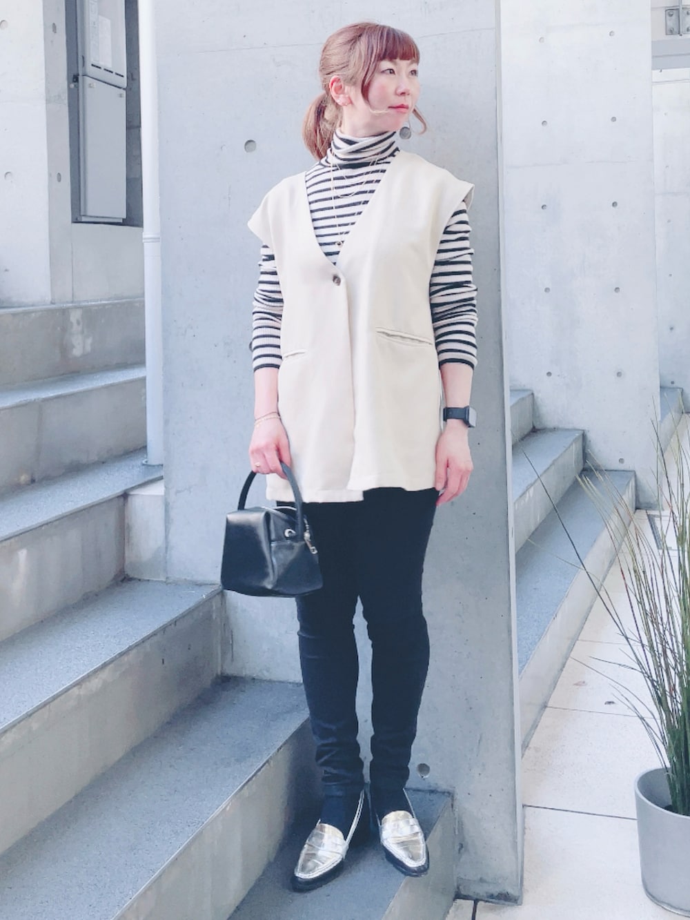 ホワイト系のベスト、ブラック系のハンドバッグ、シルバー系のローファーを着用したレディースの春コーディネートの2枚目の写真