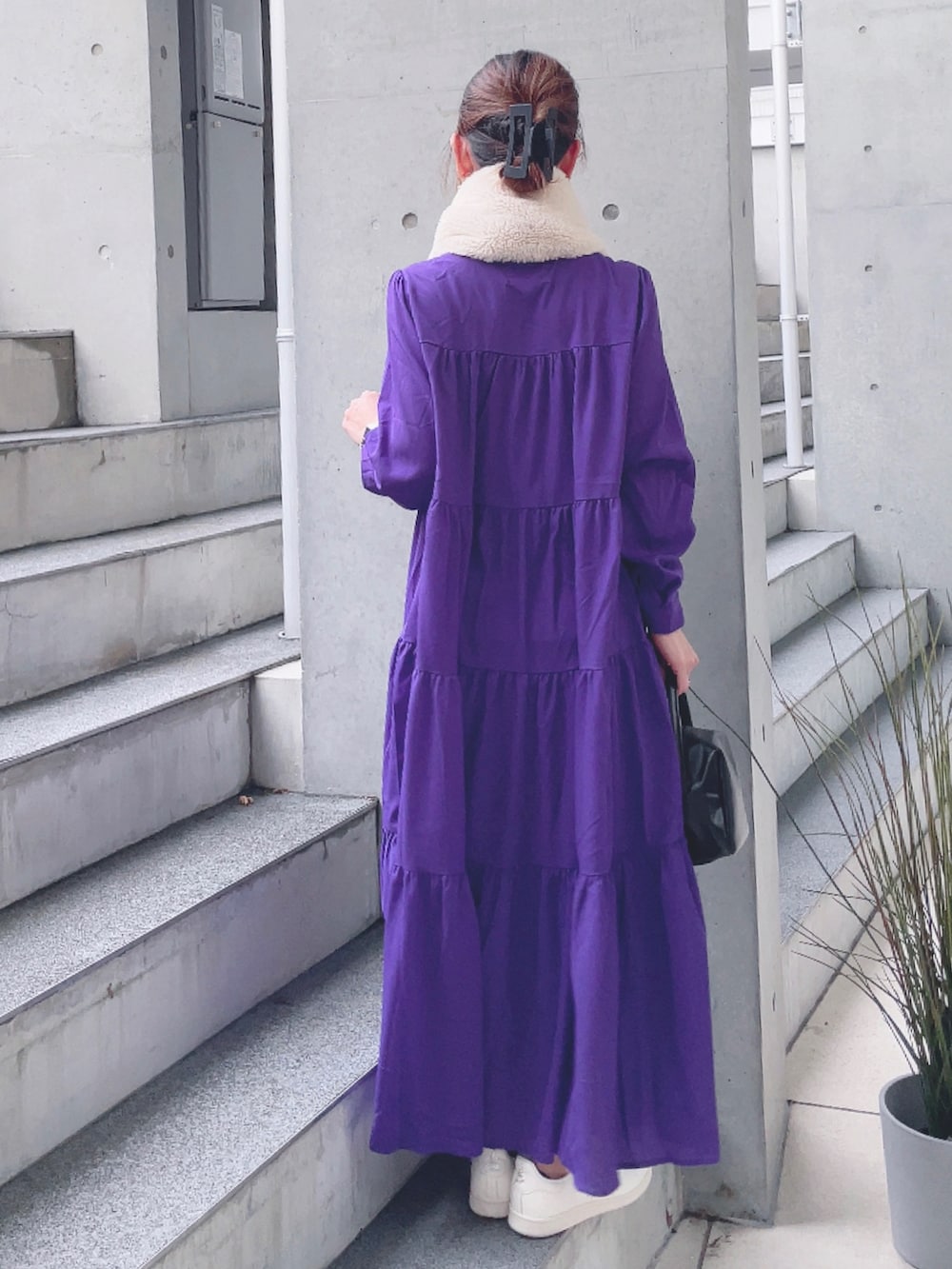 パープル系のワンピース、ブラック系のハンドバッグ、ベージュ系のスニーカーを着用したレディースの秋コーディネートの3枚目の写真