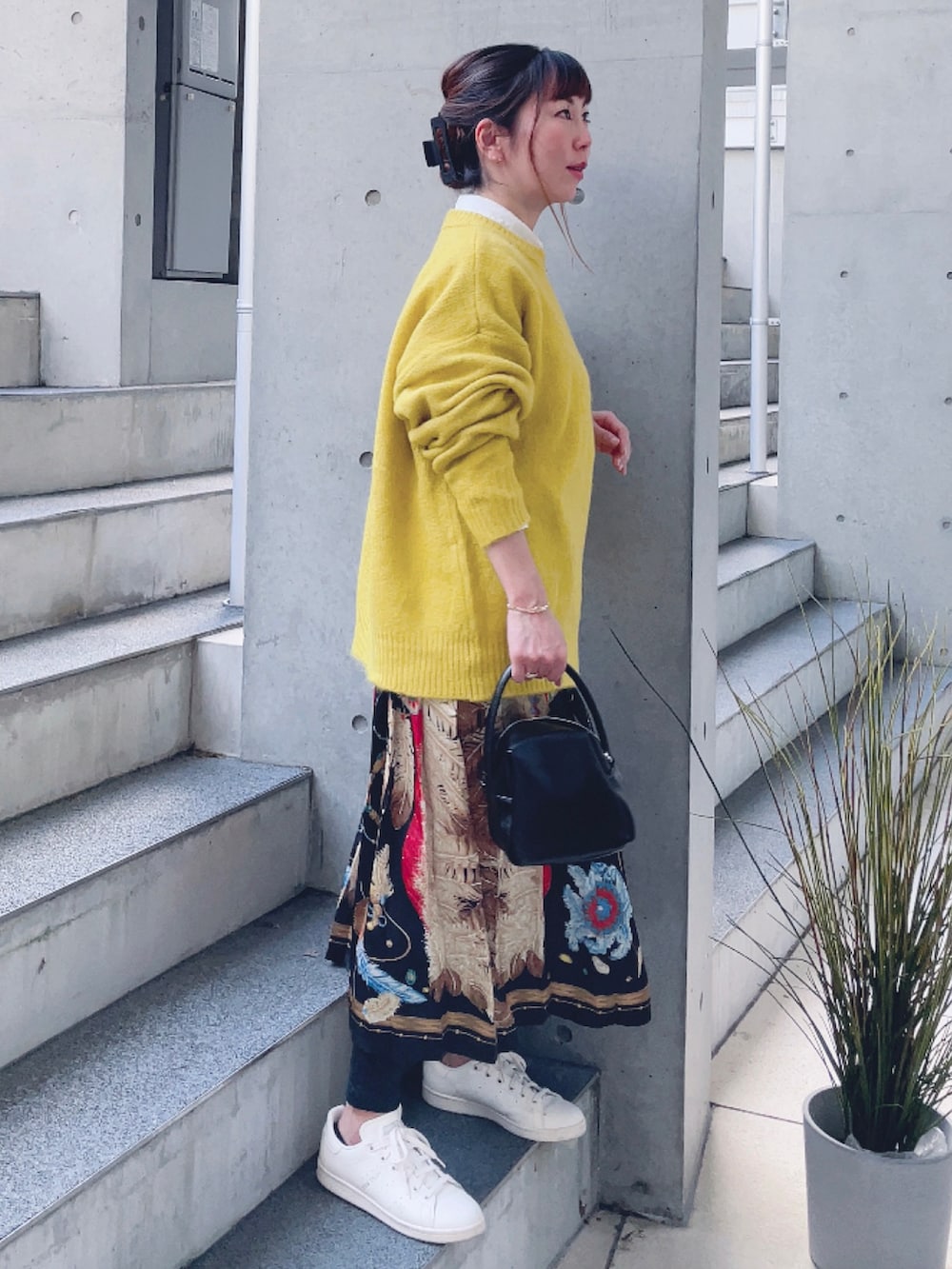 イエロー系のニット/セーター、その他のスカート、ブラック系のハンドバッグを着用したレディースの秋コーディネートの2枚目の写真