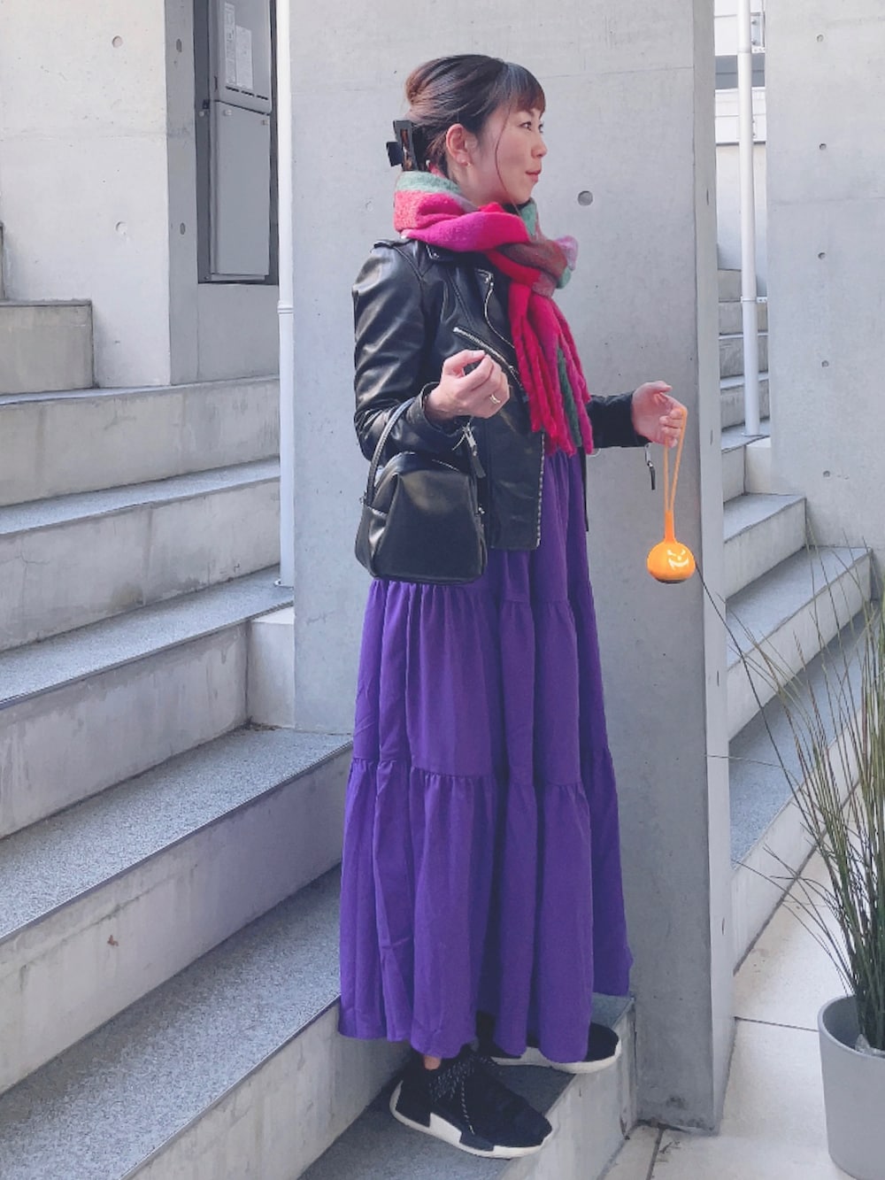 ブラック系のライダースジャケット、パープル系のワンピース、ブラック系のハンドバッグを着用したレディースの秋コーディネートの2枚目の写真
