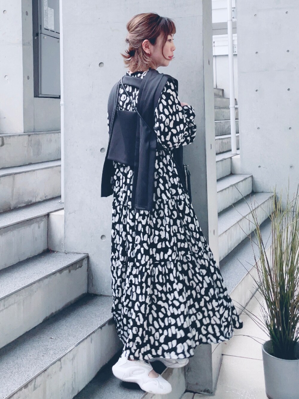 ブラック系のワンピース、ブラック系のベスト、ホワイト系のスニーカーを着用したレディースの春コーディネートの2枚目の写真