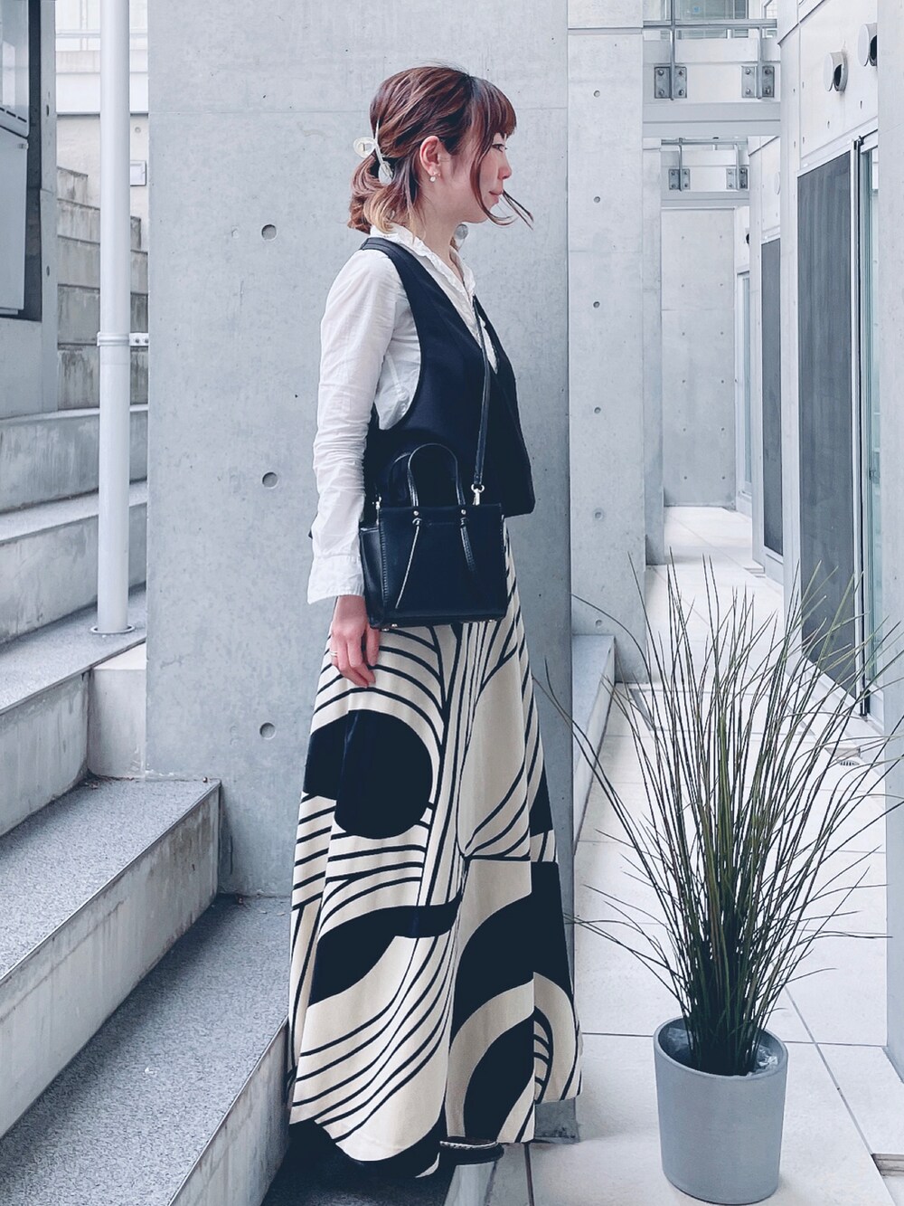 ブラック系のベスト、ホワイト系のシャツ/ブラウス、ベージュ系のスカートを着用したレディースの春コーディネートの2枚目の写真