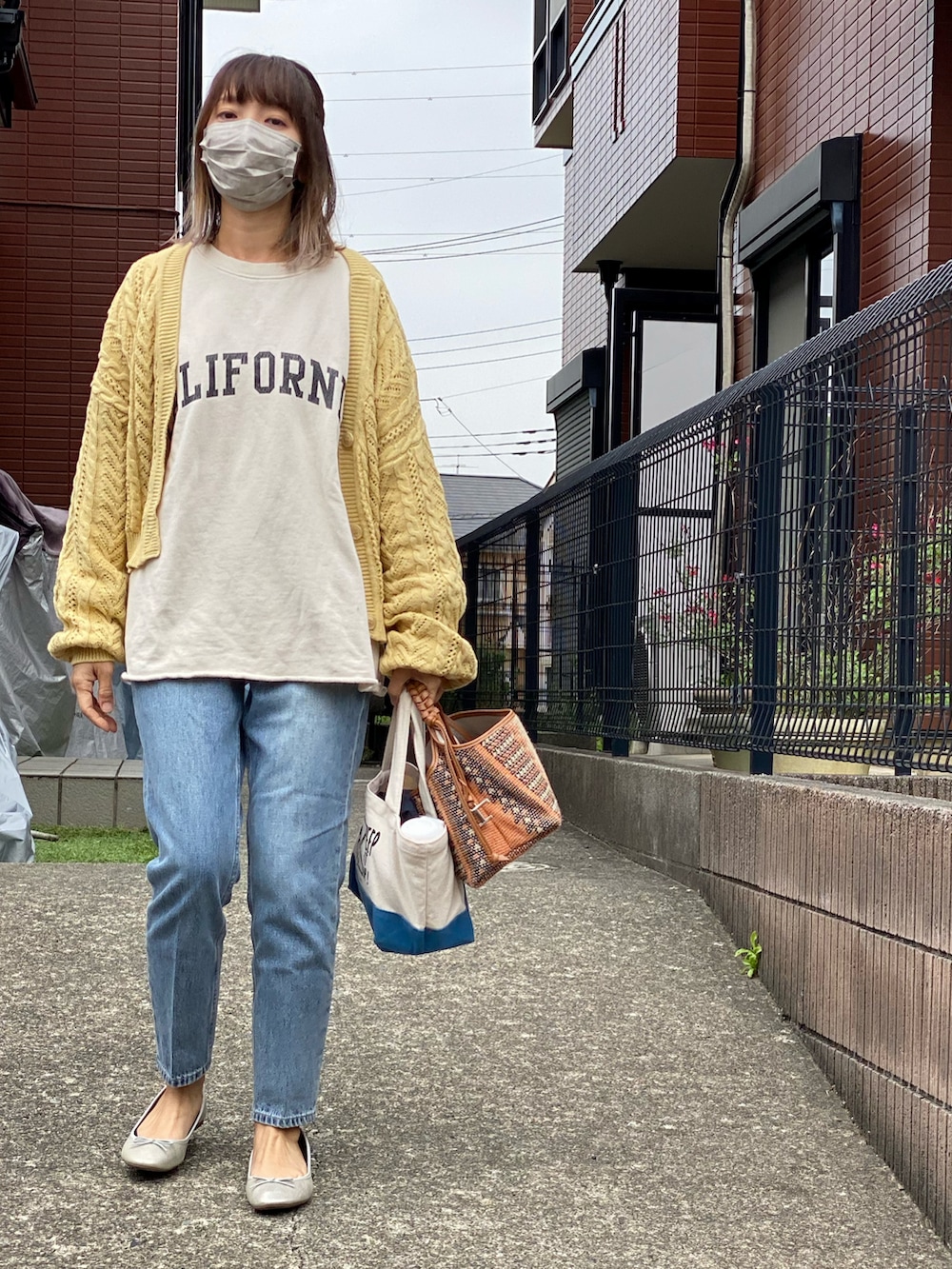 イエロー系のカーディガン/ボレロ、ブラウン系のバッグ、ブルー系のデニムパンツを着用したレディースの春コーディネートの2枚目の写真