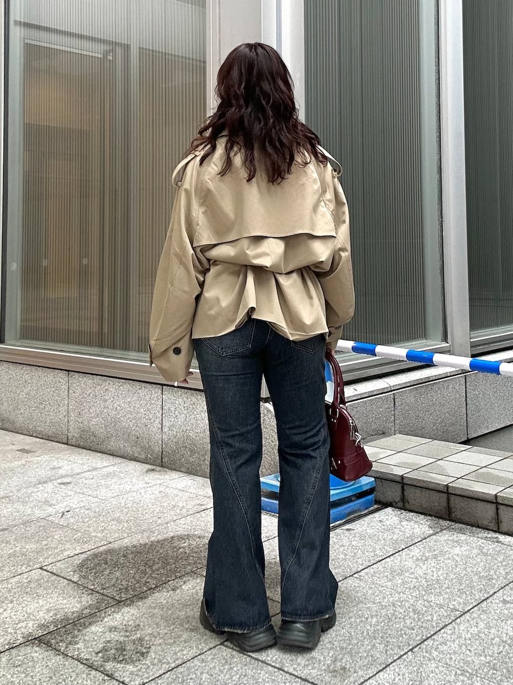 ブラック系のスニーカー、ブルー系のデニムパンツ、ベージュ系のトレンチコートを着用したレディースの秋コーディネートの4枚目の写真