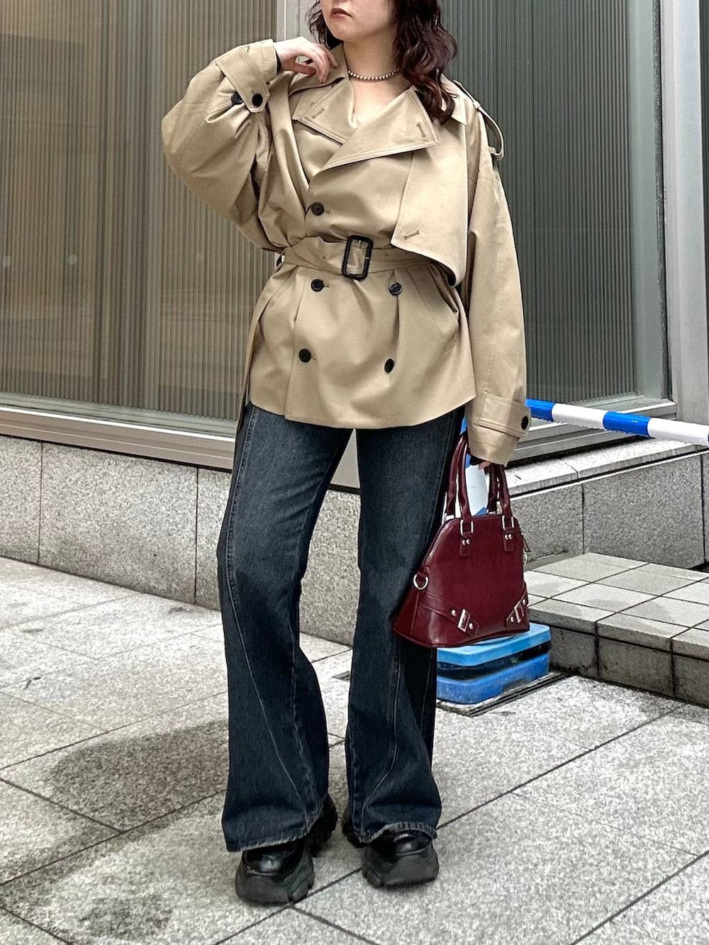 ブラック系のスニーカー、ブルー系のデニムパンツ、ベージュ系のトレンチコートを着用したレディースの秋コーディネートの2枚目の写真