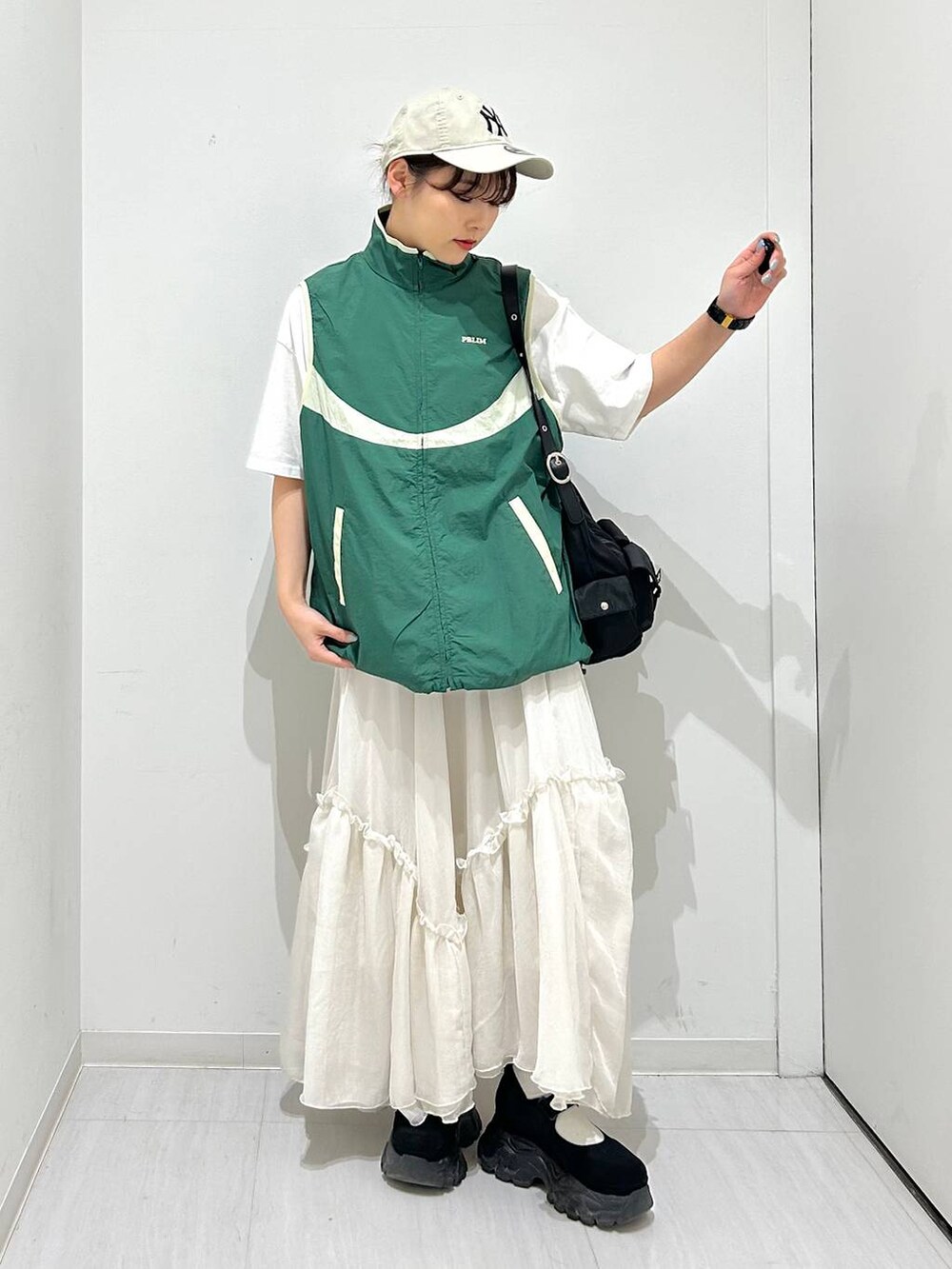 ブラック系のショルダーバッグ、グリーン系のベスト、ホワイト系のスカートを着用したレディースの春コーディネートの3枚目の写真