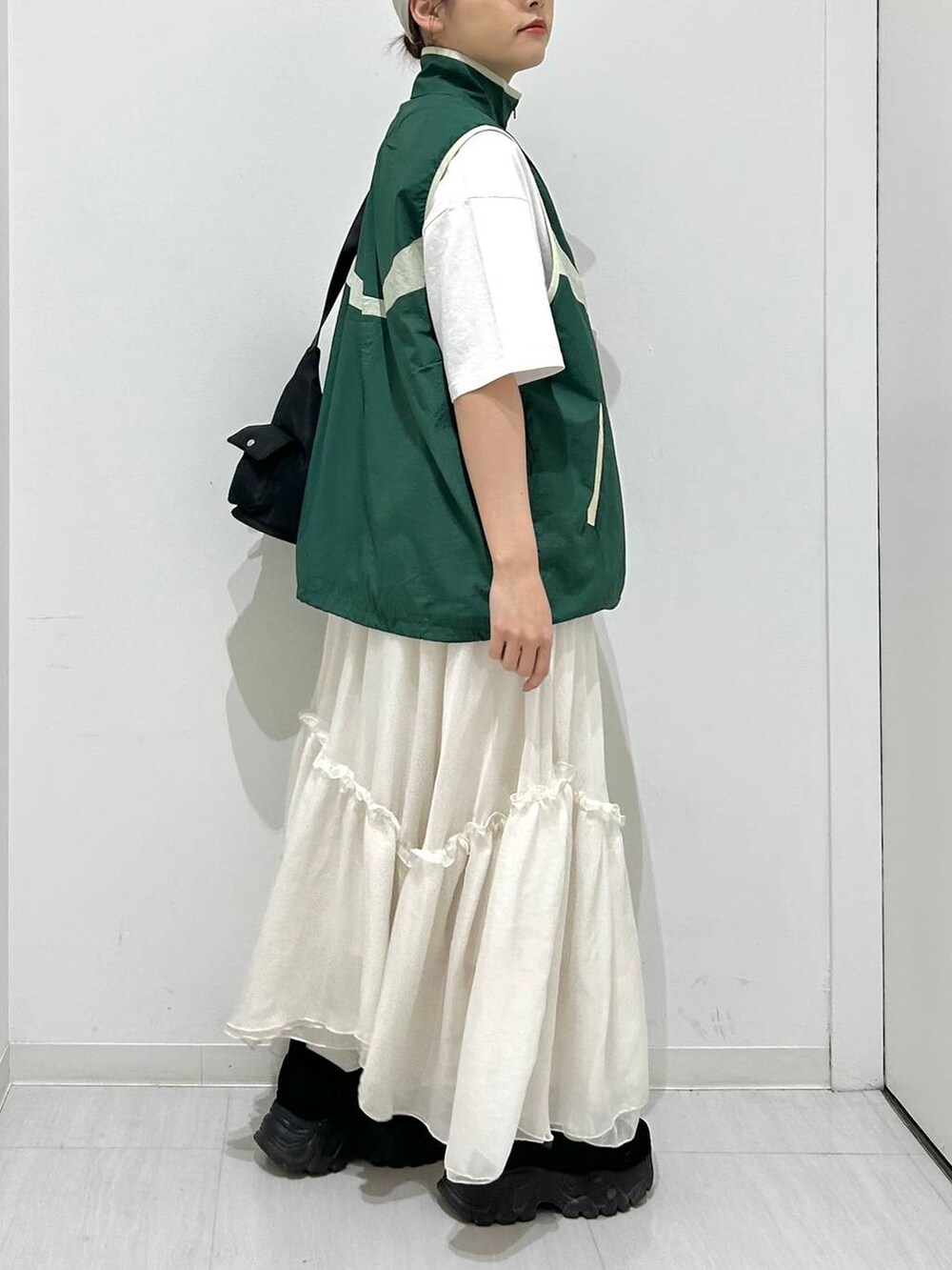ブラック系のショルダーバッグ、グリーン系のベスト、ホワイト系のスカートを着用したレディースの春コーディネートの6枚目の写真