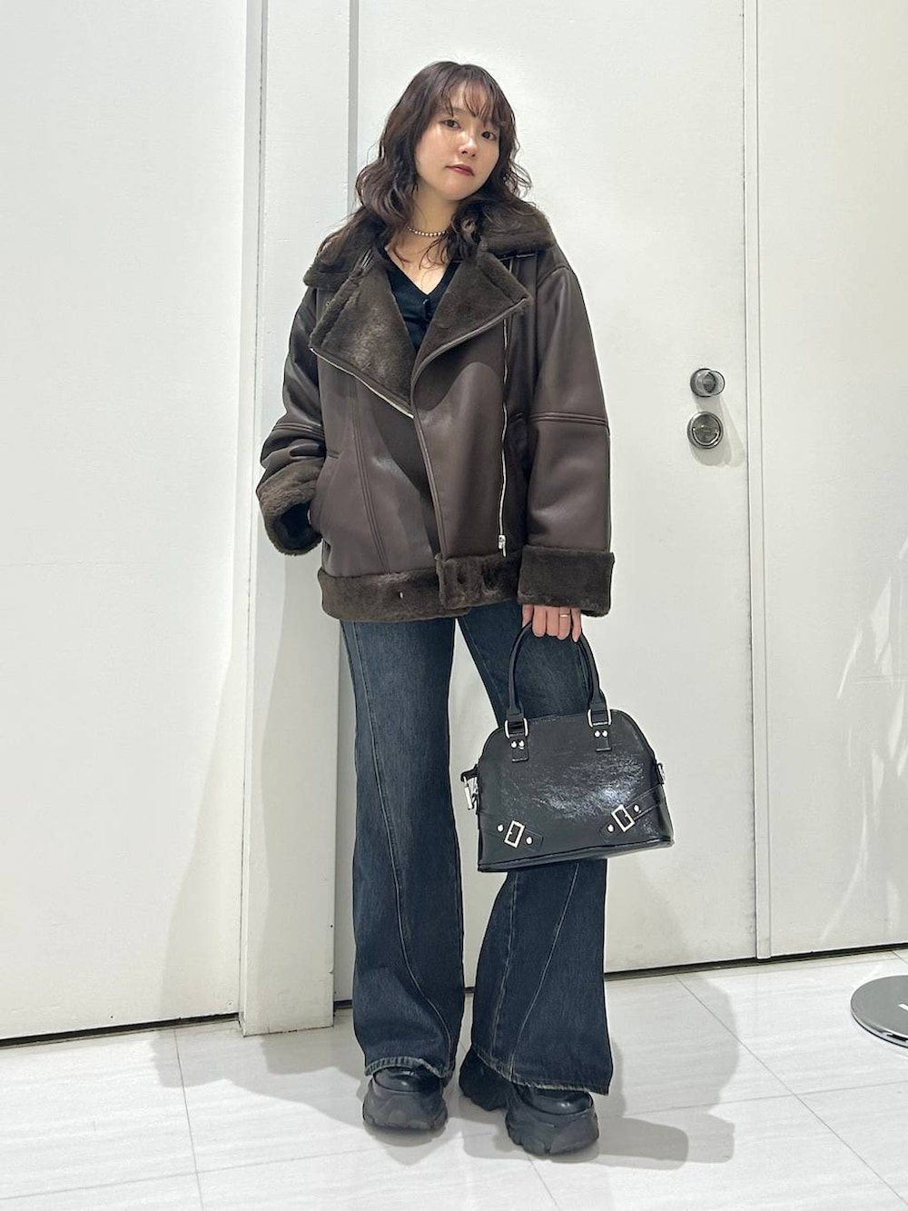 ブラック系のスニーカー、ブラック系のショルダーバッグ、ブルー系のデニムパンツを着用したレディースの秋コーディネートの2枚目の写真