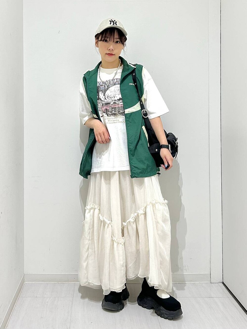 グリーン系のベスト、ホワイト系のスカート、ホワイト系のTシャツ/カットソーを着用したレディースの春コーディネートの2枚目の写真