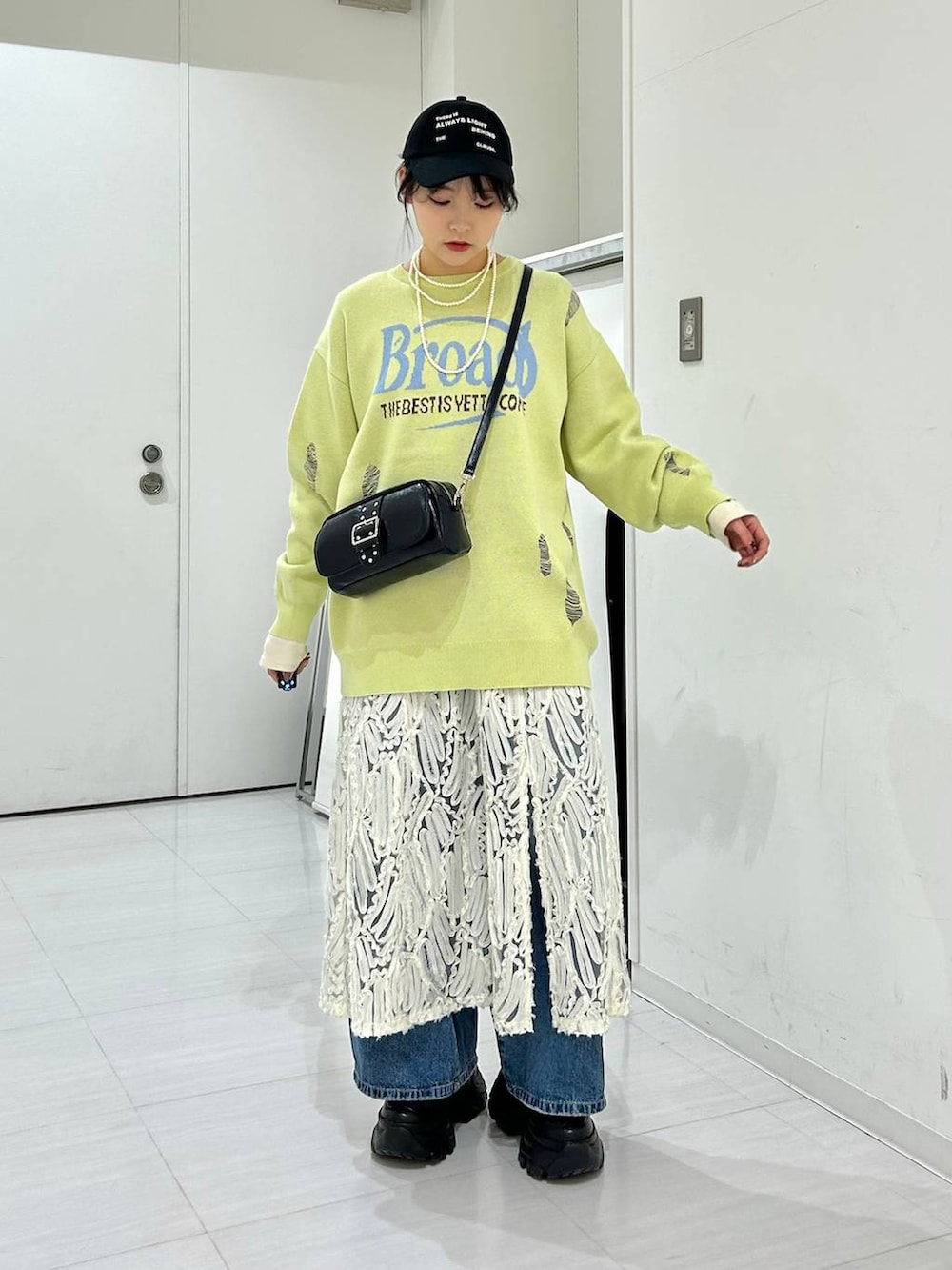 ブルー系のデニムパンツ、ホワイト系のワンピース、イエロー系のニット/セーターを着用したレディースの冬コーディネートの2枚目の写真