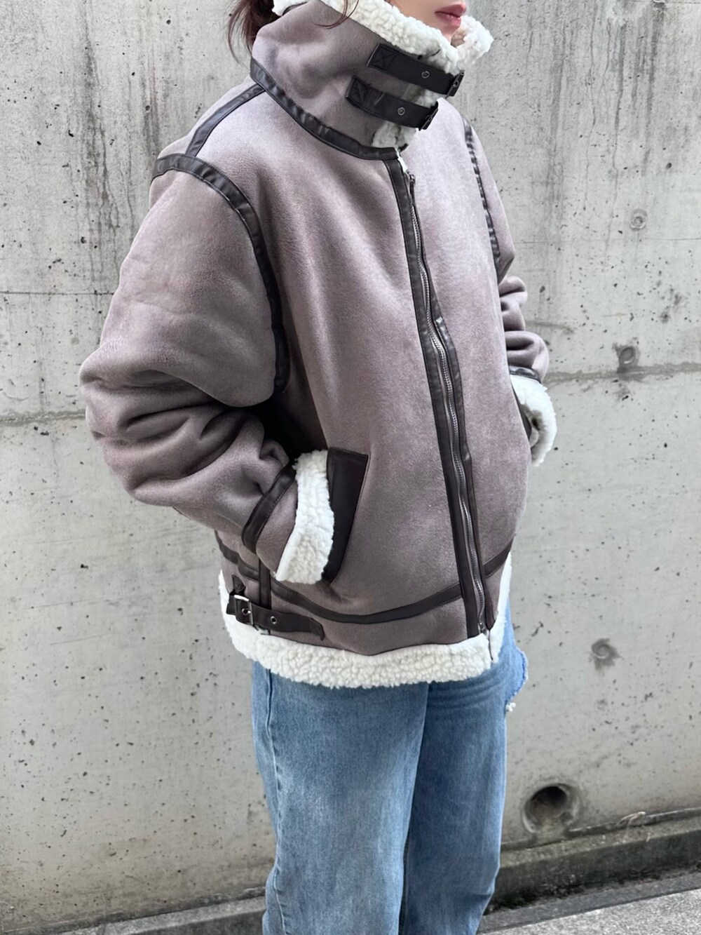 グレー系のムートンコート、ホワイト系のニット/セーター、ブルー系のデニムパンツを着用したレディースの冬コーディネートの3枚目の写真