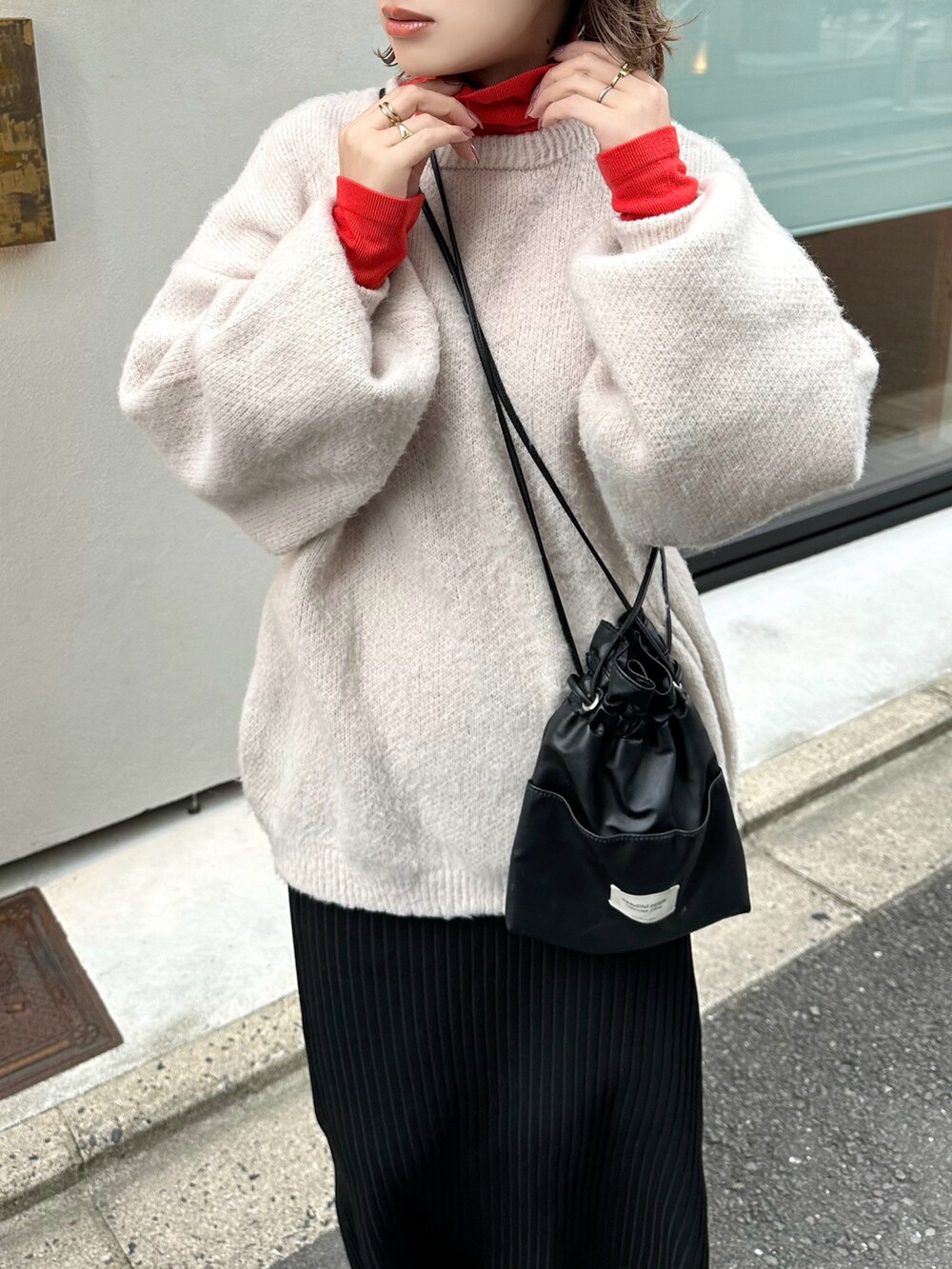 ベージュ系のニット/セーター、オレンジ系のトップス、ブラック系のスカートを着用したレディースの冬コーディネートの4枚目の写真