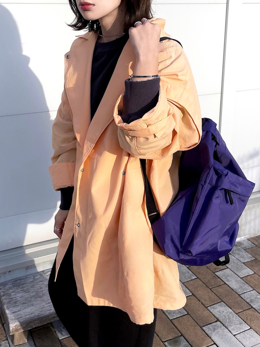 オレンジ系のポンチョ、グレー系のTシャツ/カットソー、ブラック系のパンツを着用したレディースの春コーディネートの4枚目の写真