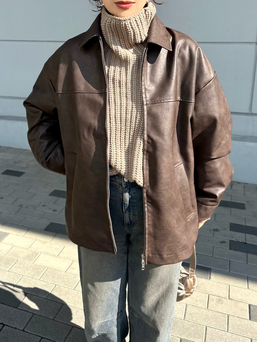 ブラウン系のブルゾン、ベージュ系のニット/セーター、ブルー系のデニムパンツを着用したレディースの冬コーディネートの5枚目の写真