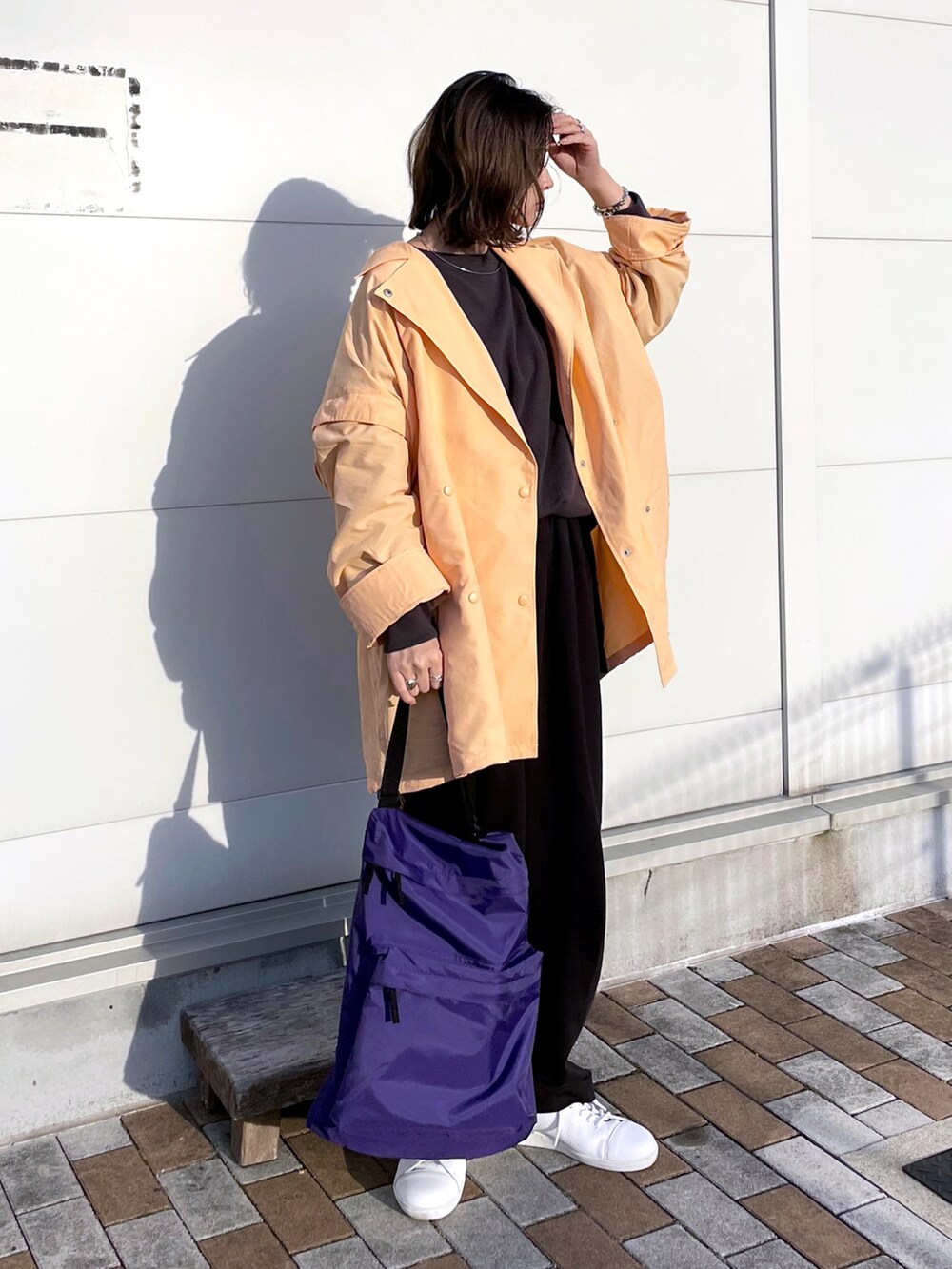 オレンジ系のポンチョ、グレー系のTシャツ/カットソー、ブラック系のパンツを着用したレディースの春コーディネートの2枚目の写真