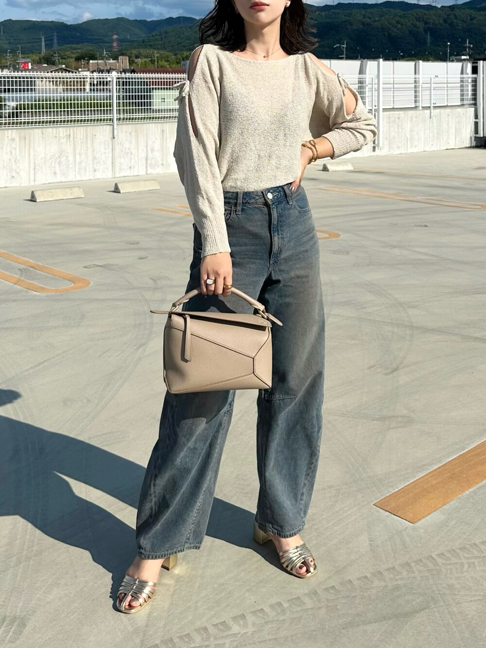 ベージュ系のニット/セーター、ブルー系のデニムパンツ、ベージュ系のショルダーバッグを着用したレディースの夏コーディネートの3枚目の写真